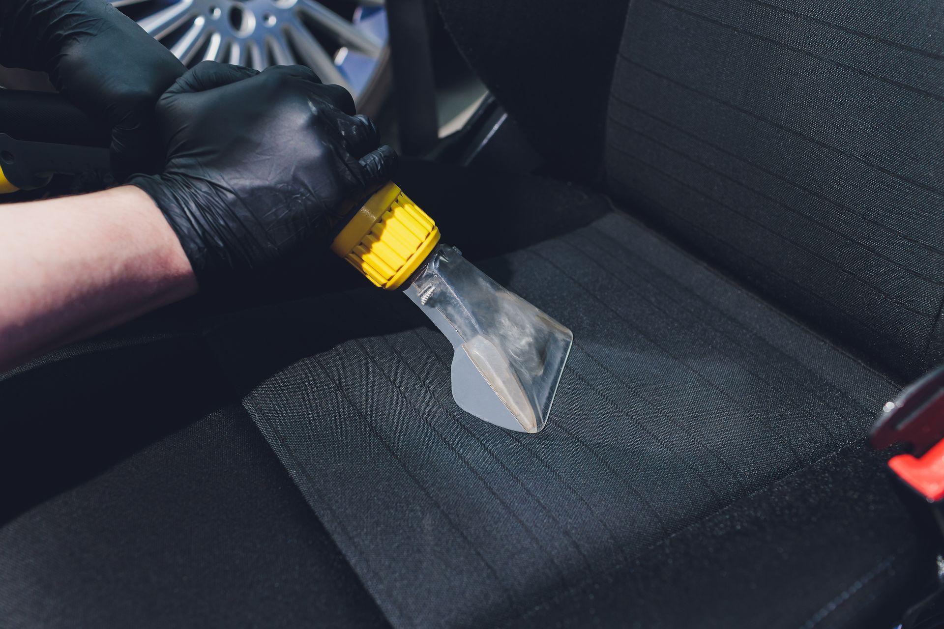 hand wearing black vinyl glove uses an upholstery cleaner to clean and disinfect car seats