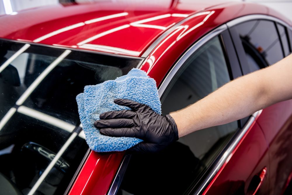 A person is cleaning a red car with a blue cloth.