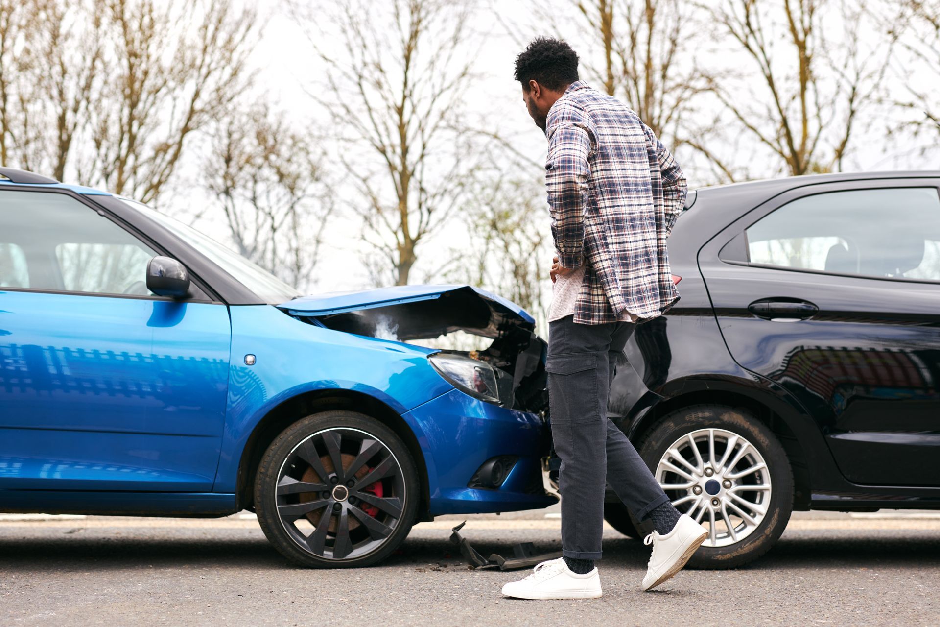 A man is standing between two cars that have been involved in a car accident, identifying damage to the rearend