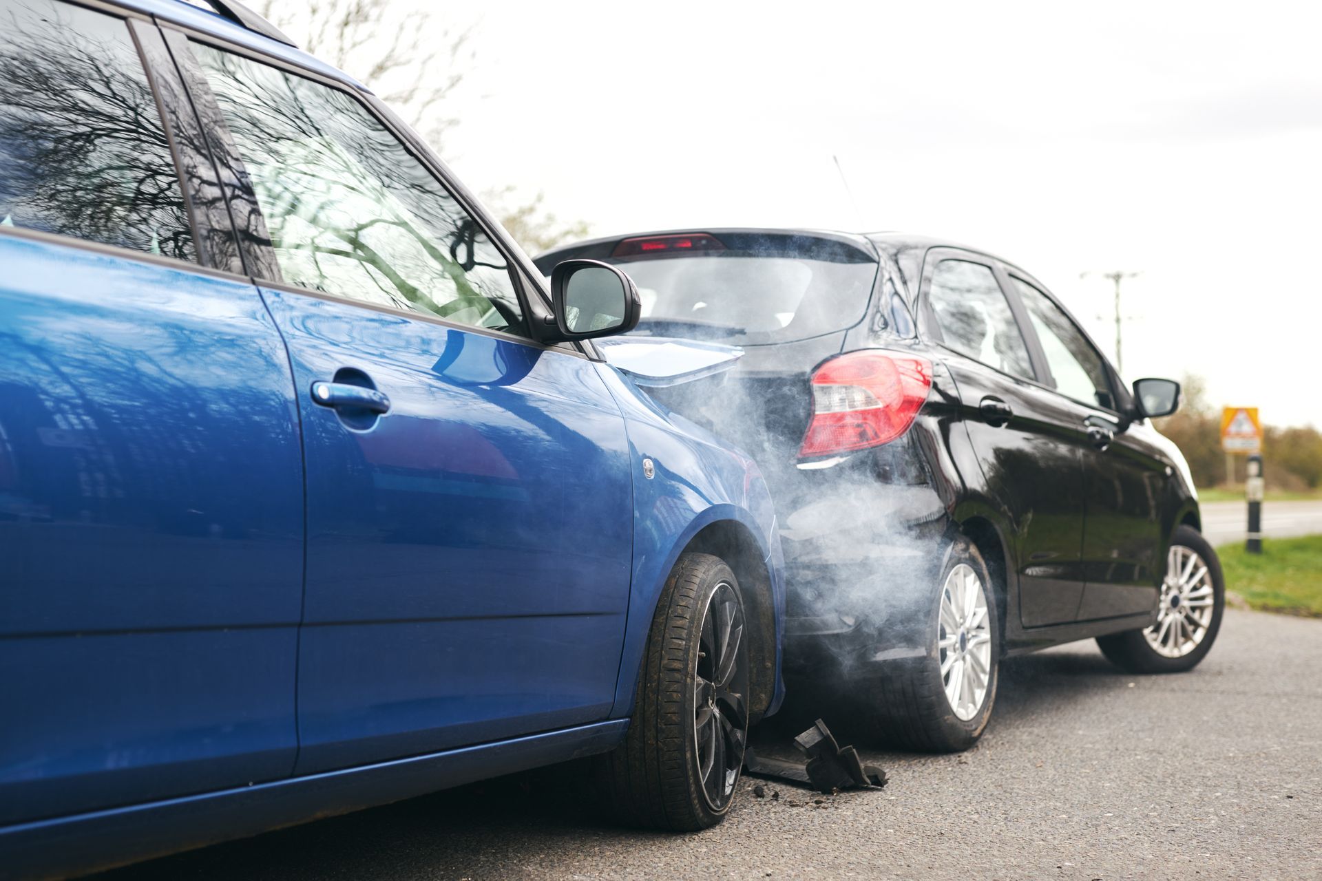 Two cars are involved in a car accident on the side of the road, with damage to the rearend