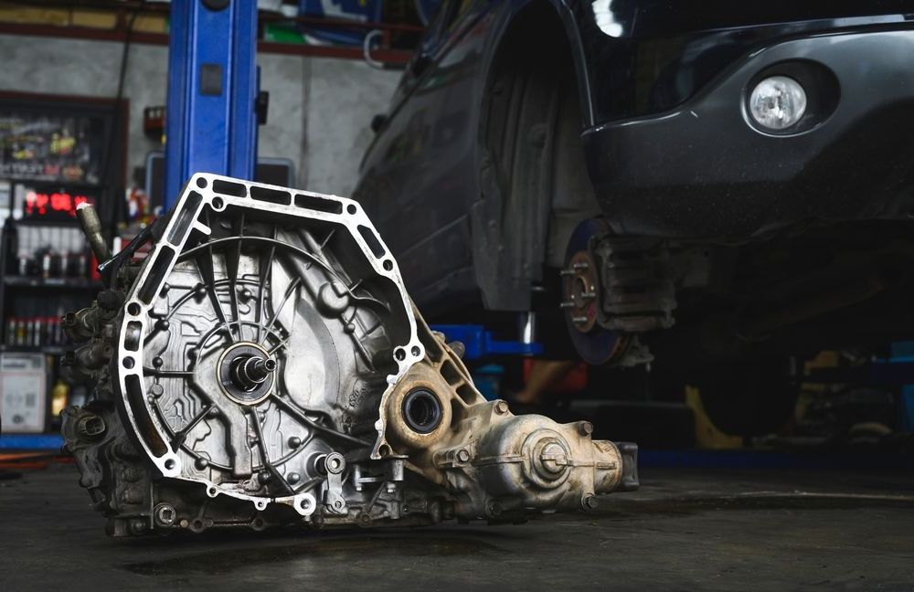 A car is being repaired in a garage with a gearbox on a lift.