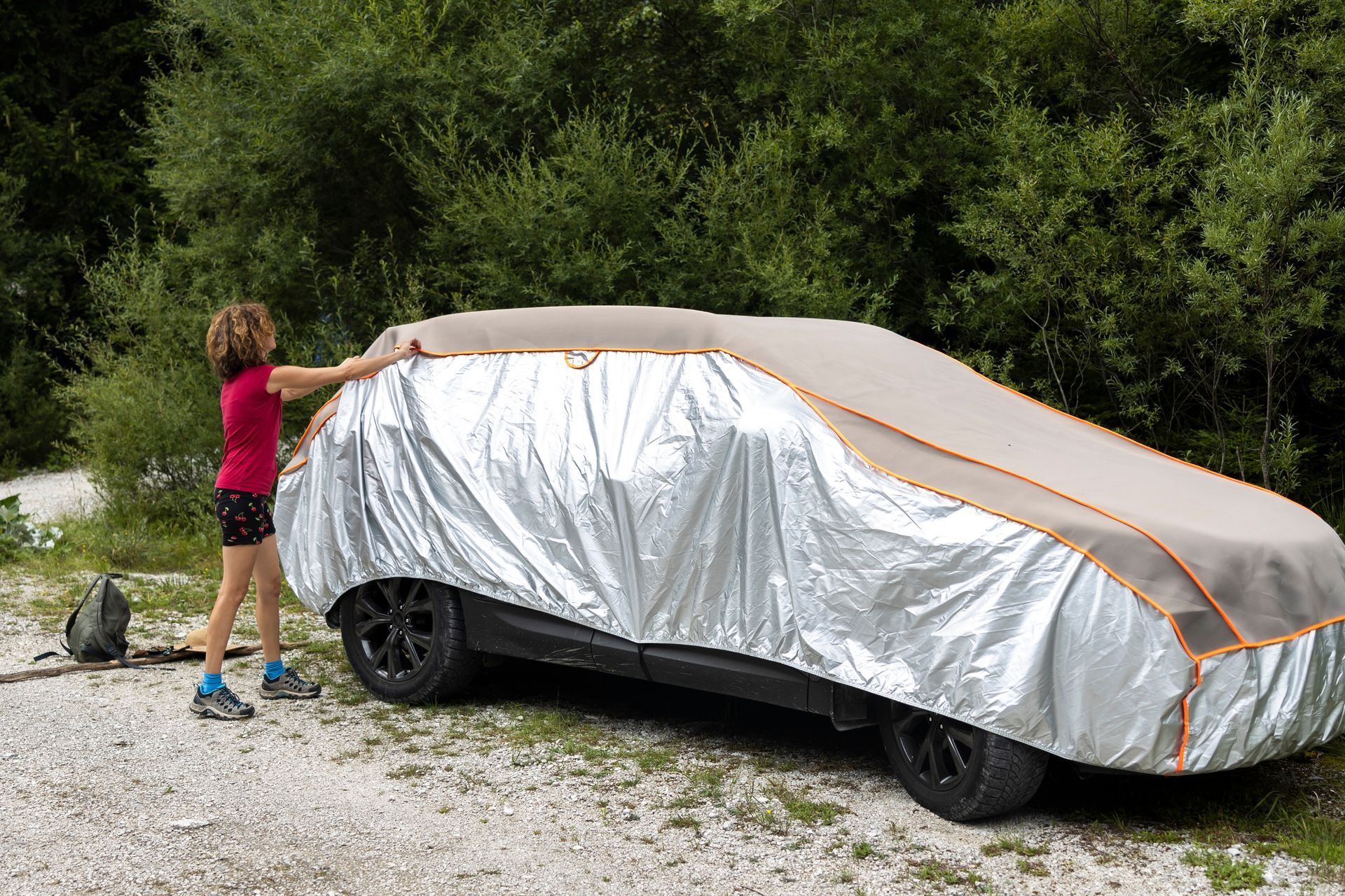 A woman is putting a hail car cover on a car.