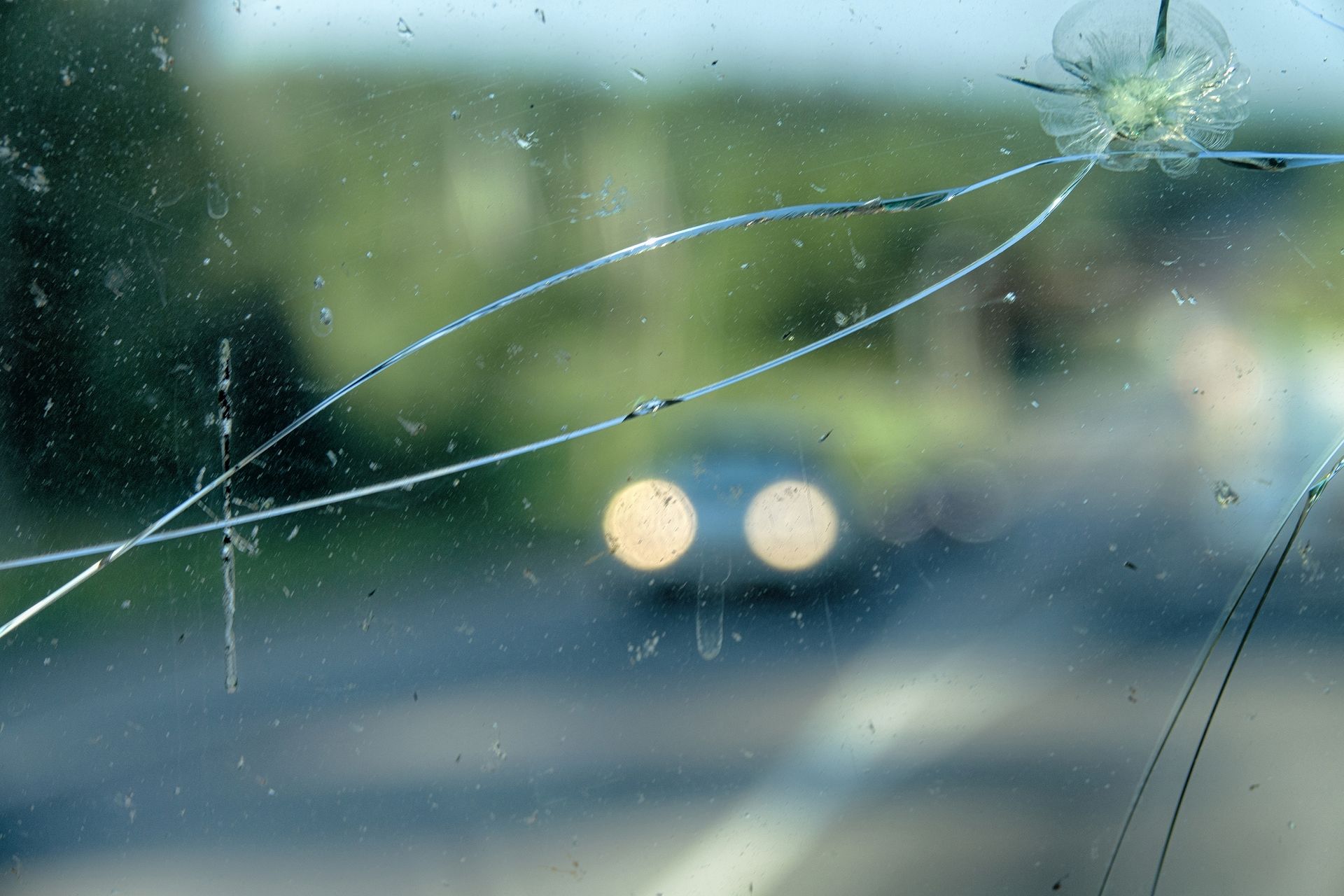 A close up of a broken windshield with a car in the background.