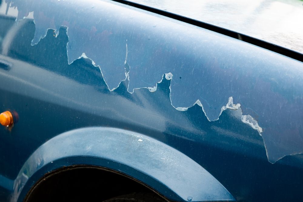 A close up of a blue car with peeling paint.