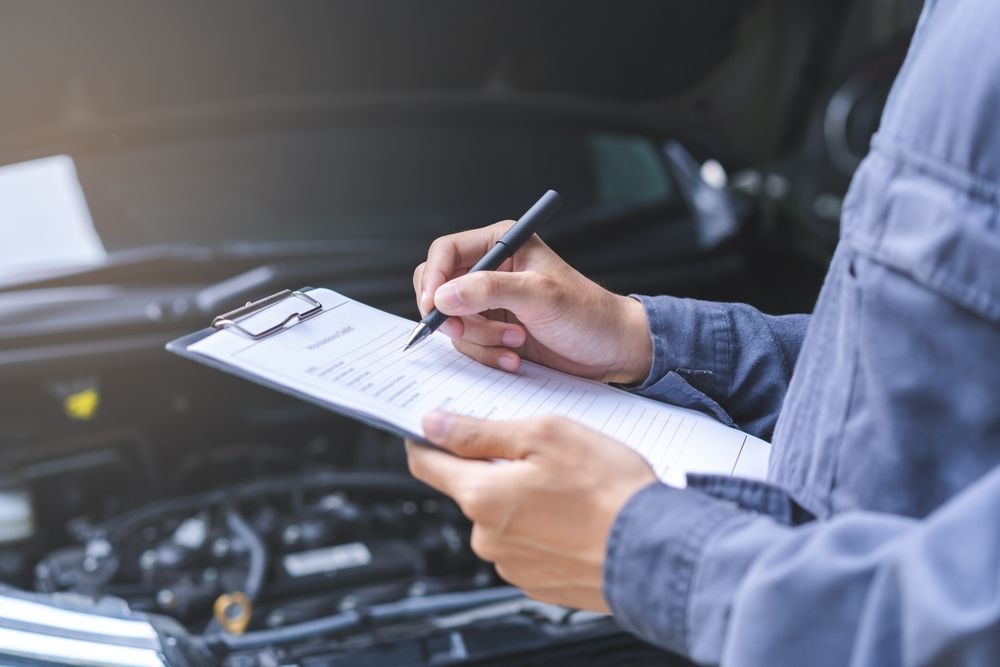 A mechanic is writing on a clipboard in front of a car.