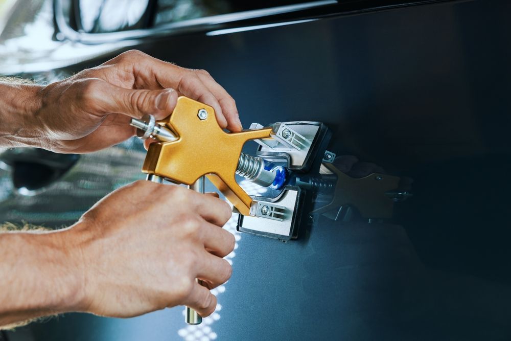 A man is using a tool to fix a scratch on a car.