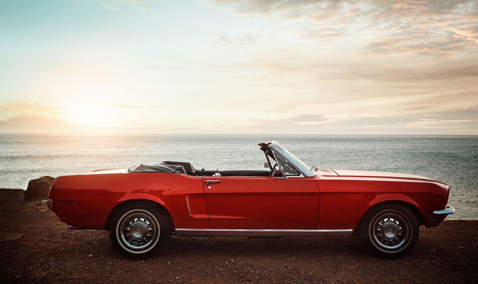 A red convertible mustang is parked on the beach at sunset.