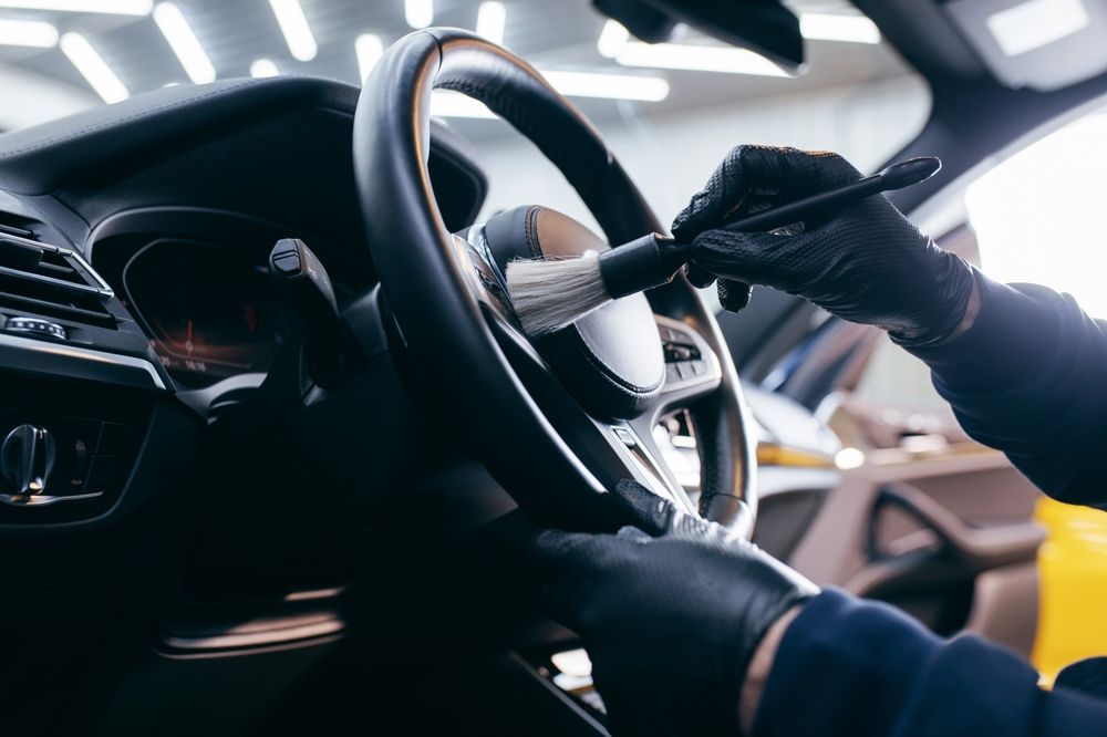 Hands in black gloves cleaning car steering wheel with a brush.