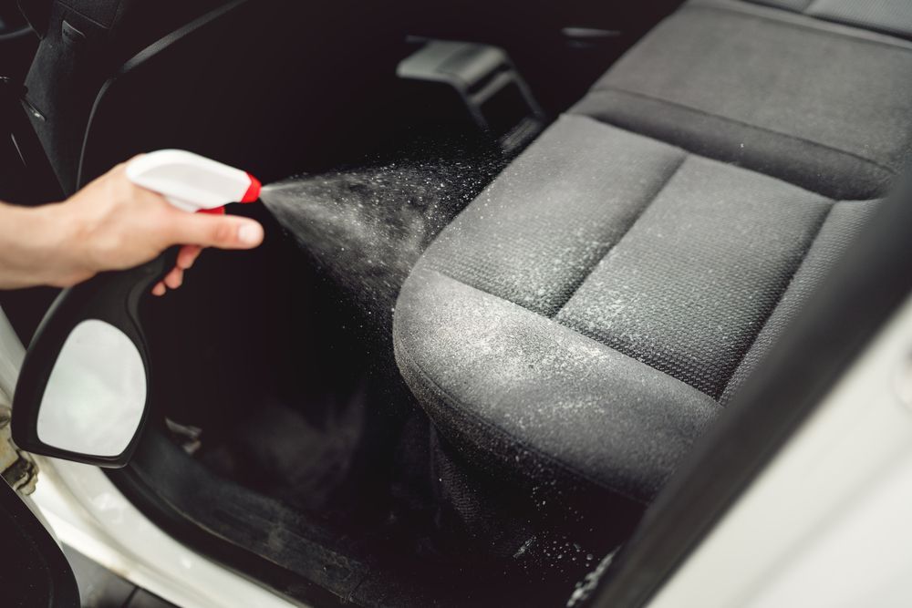 person cleaning car seat stain with spray cleaner