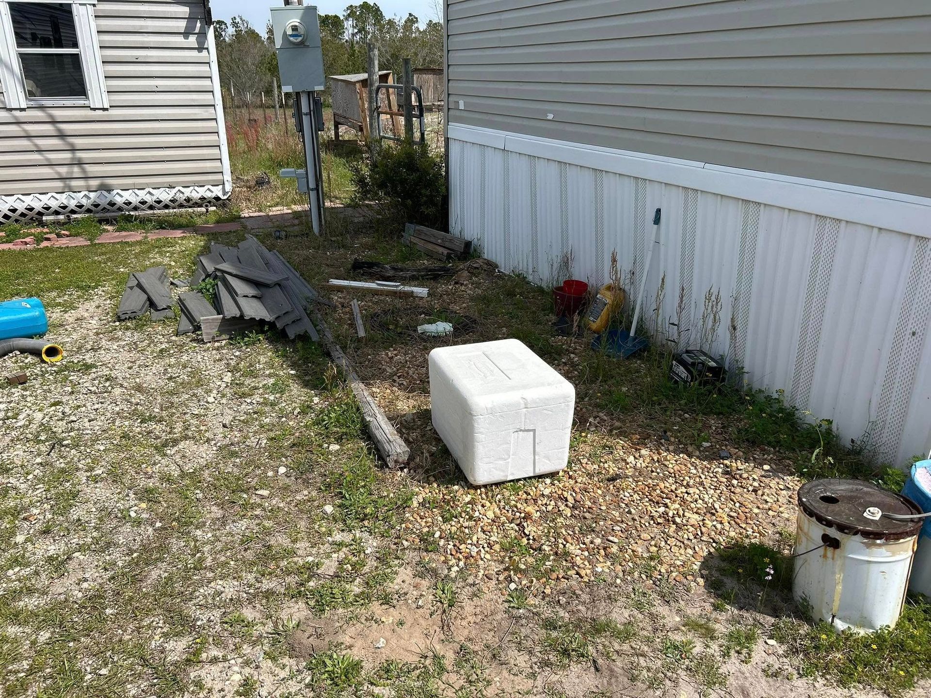 Exterior view: Side of a mobile home and yard with debris, a white box, and a utility pole.