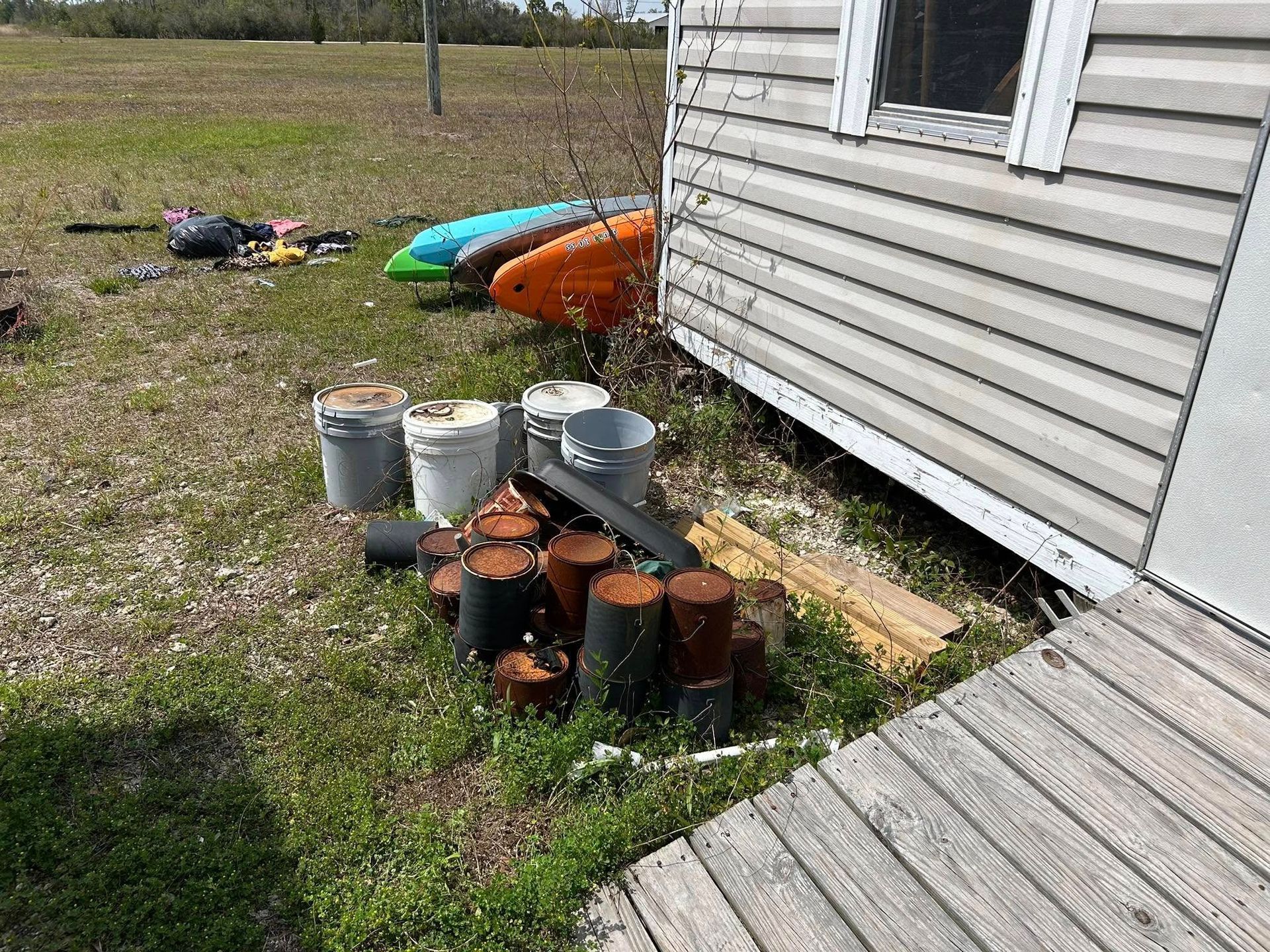 Backyard scene with kayaks, buckets, pots, and a weathered building.