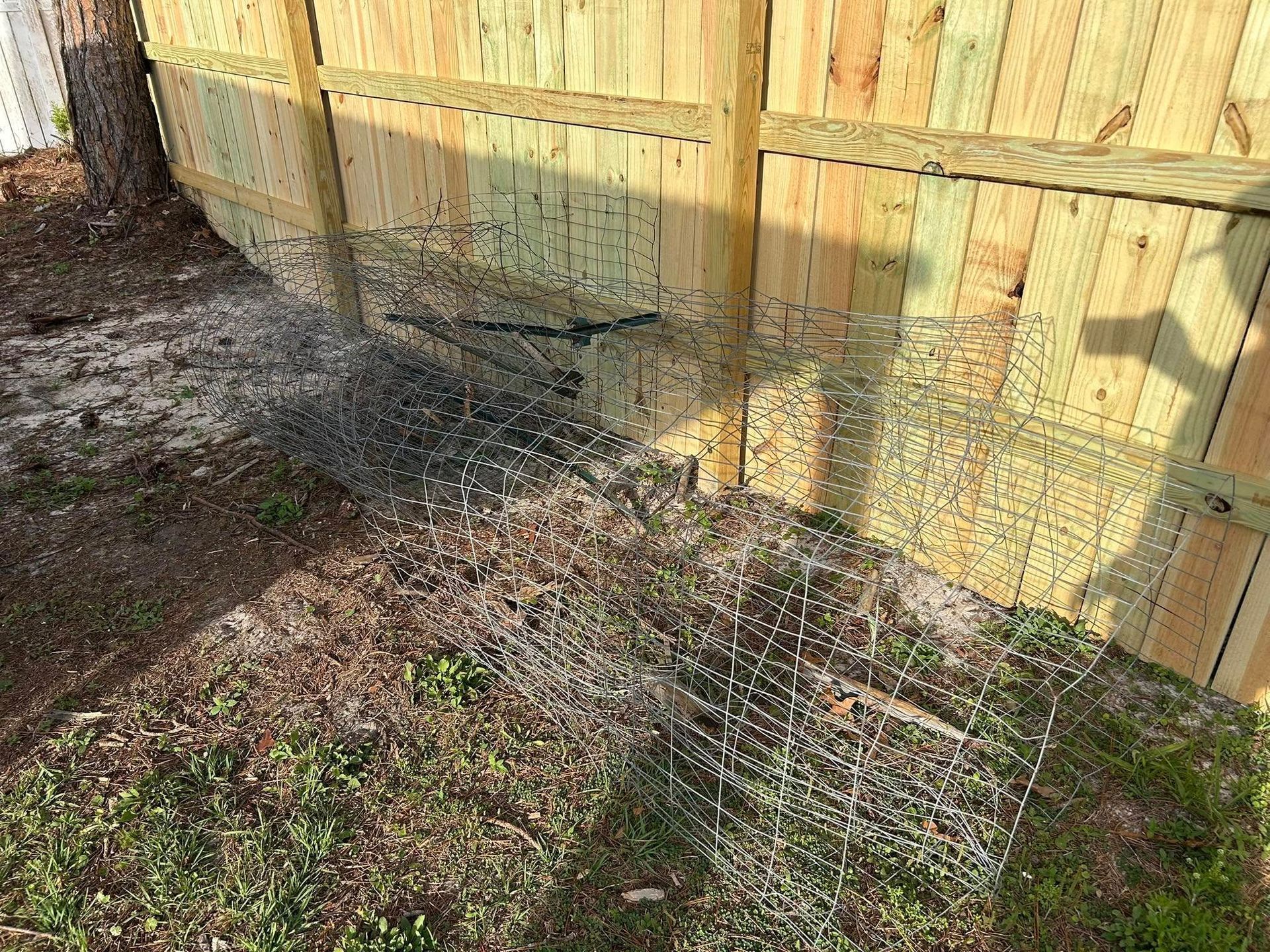 Wire mesh attached to a wooden fence, covering a gap.