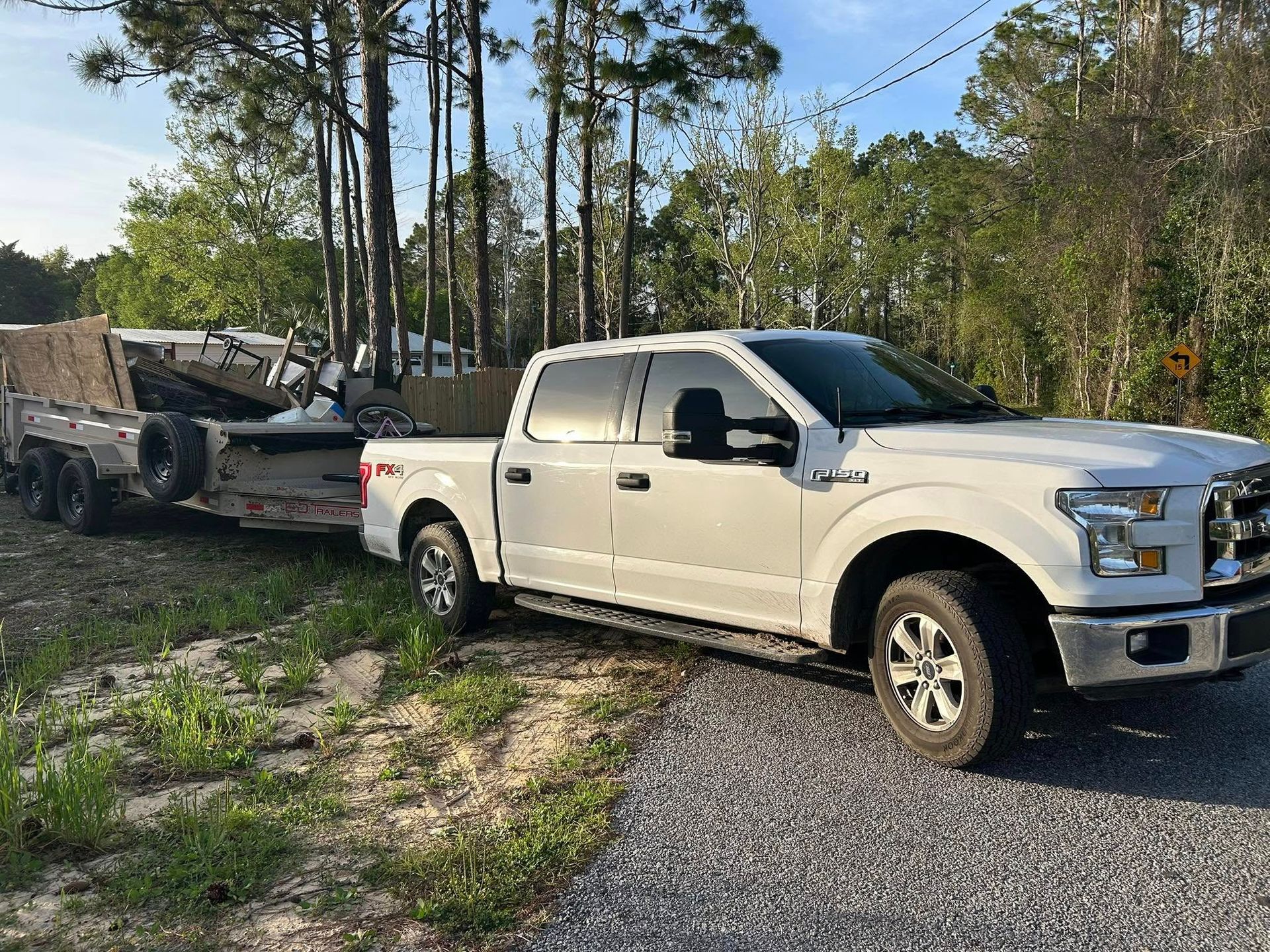 White pickup truck towing a trailer on a gravel road, with trees in the background.