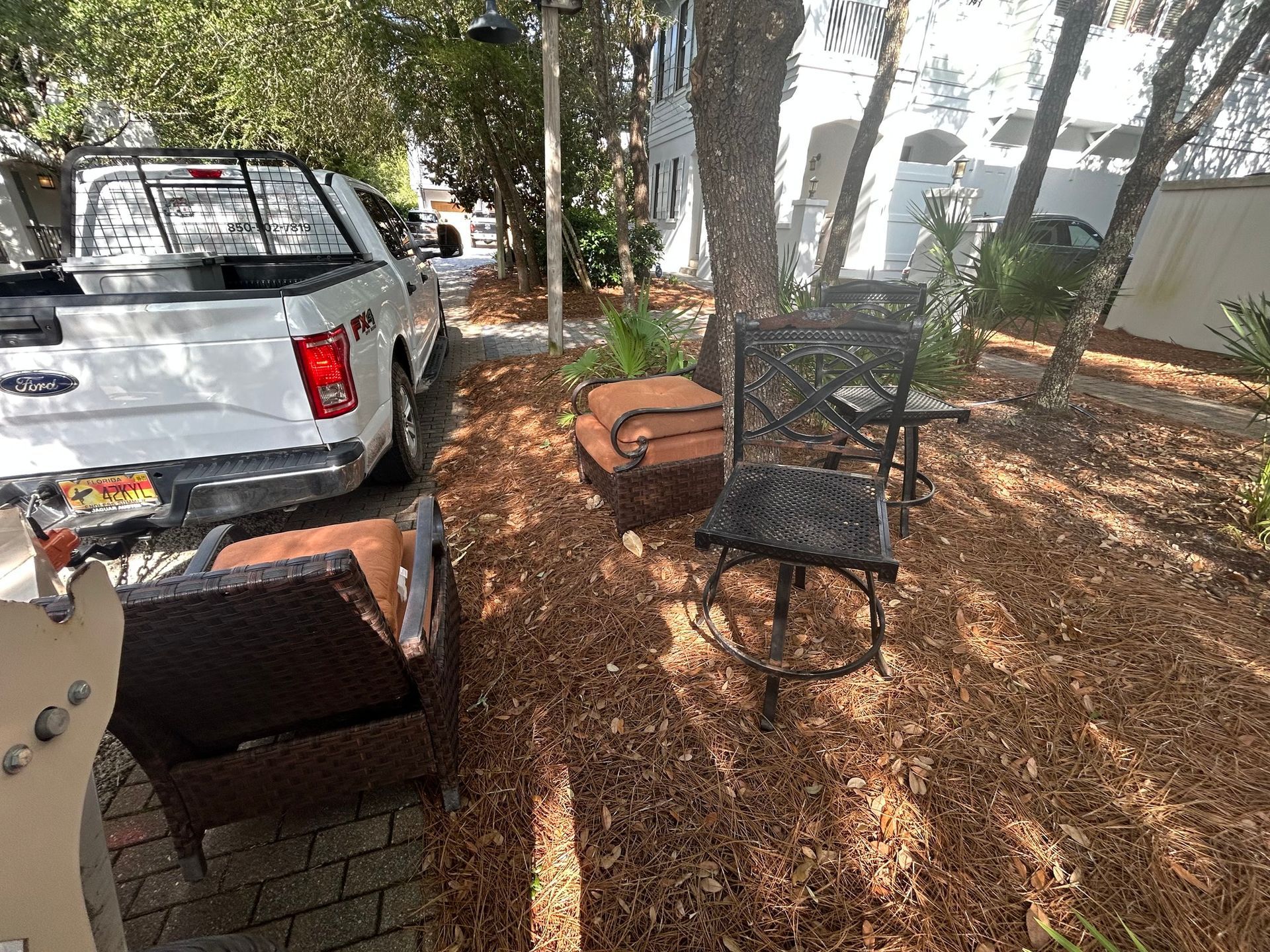 White truck parked near patio furniture on a mulch bed, under a tree.