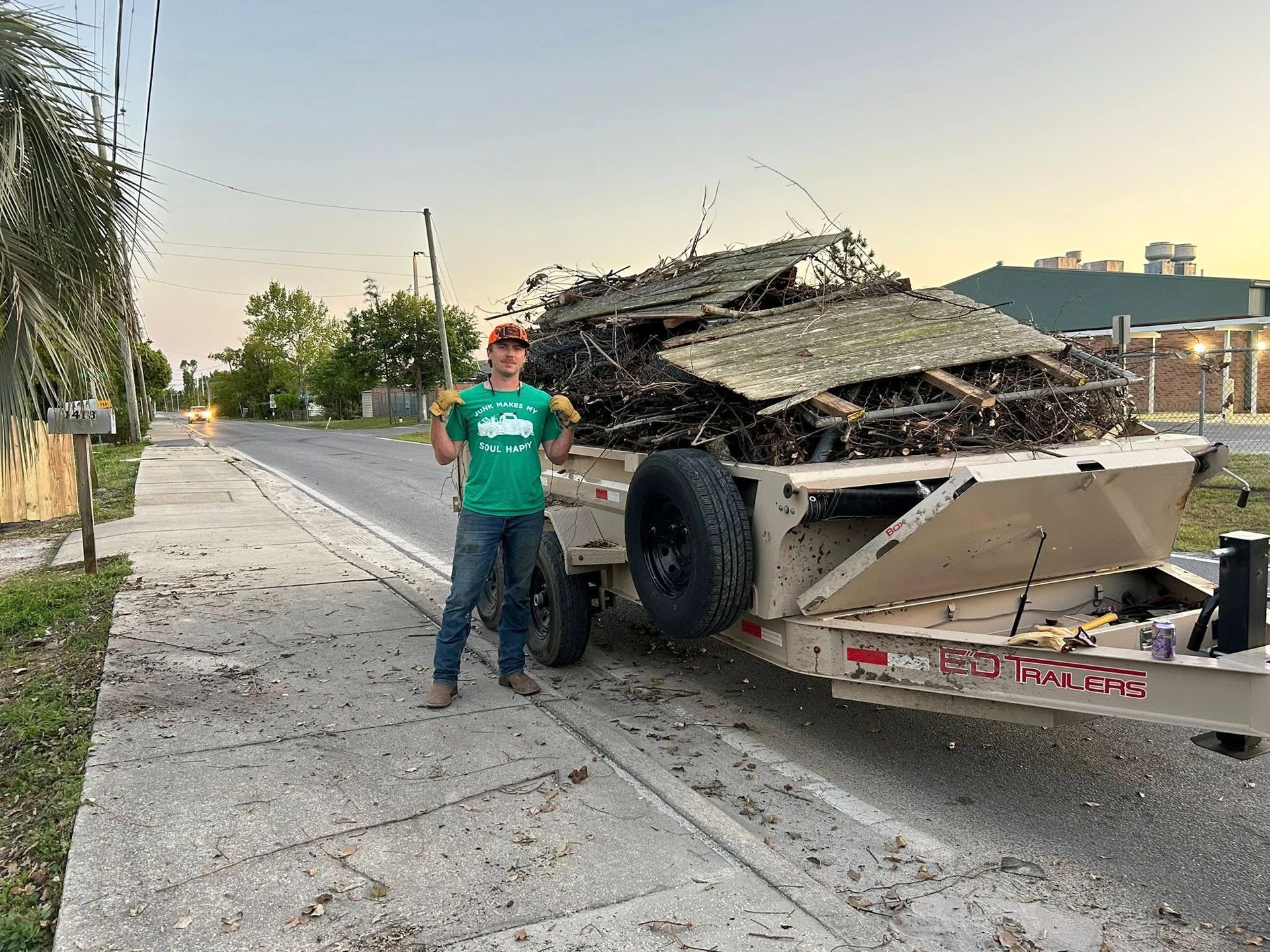 Person standing next to a trailer overflowing with debris on a city street.