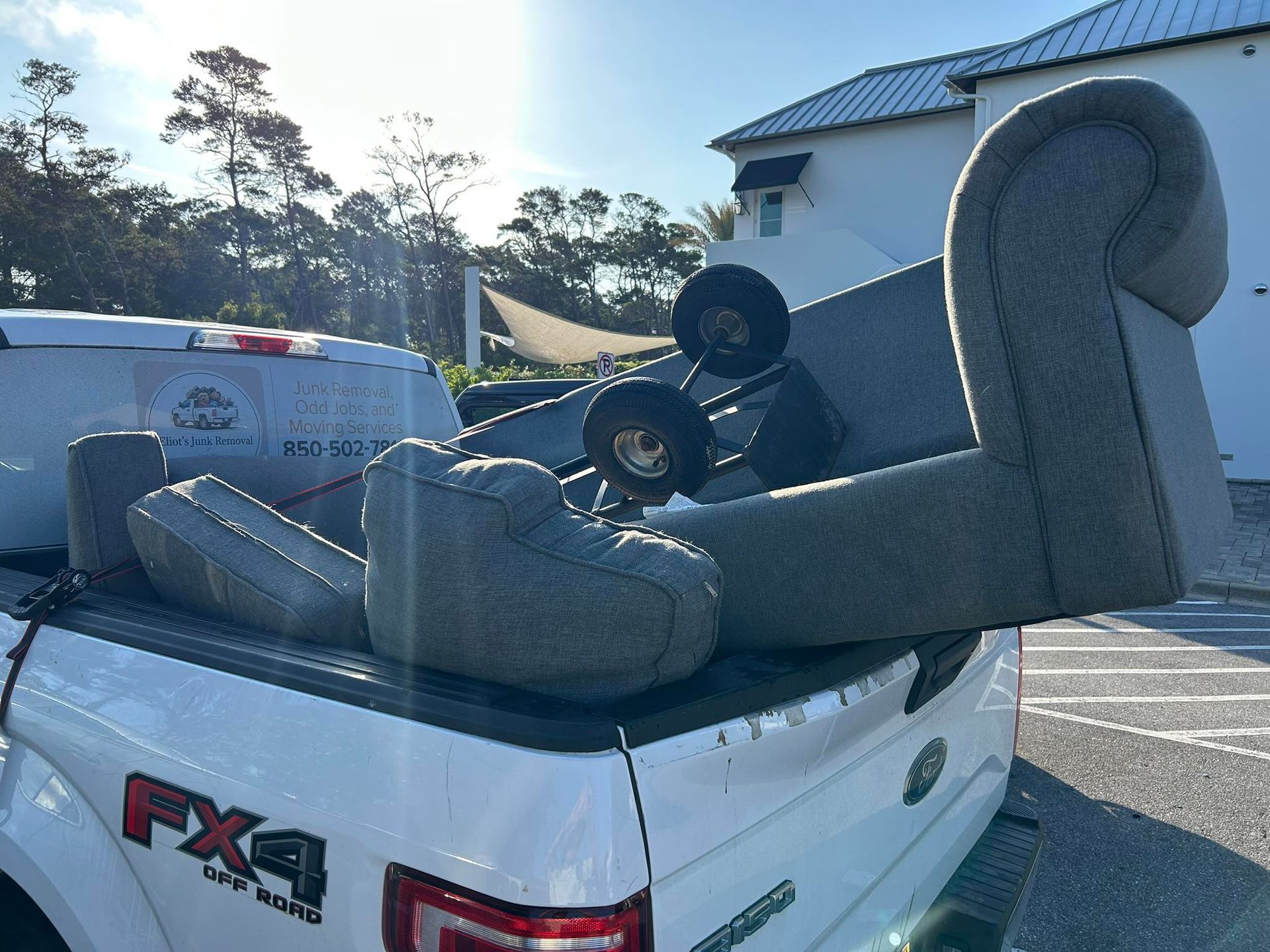 Grey couch pieces loaded in a white pickup truck. Exterior daytime shot.