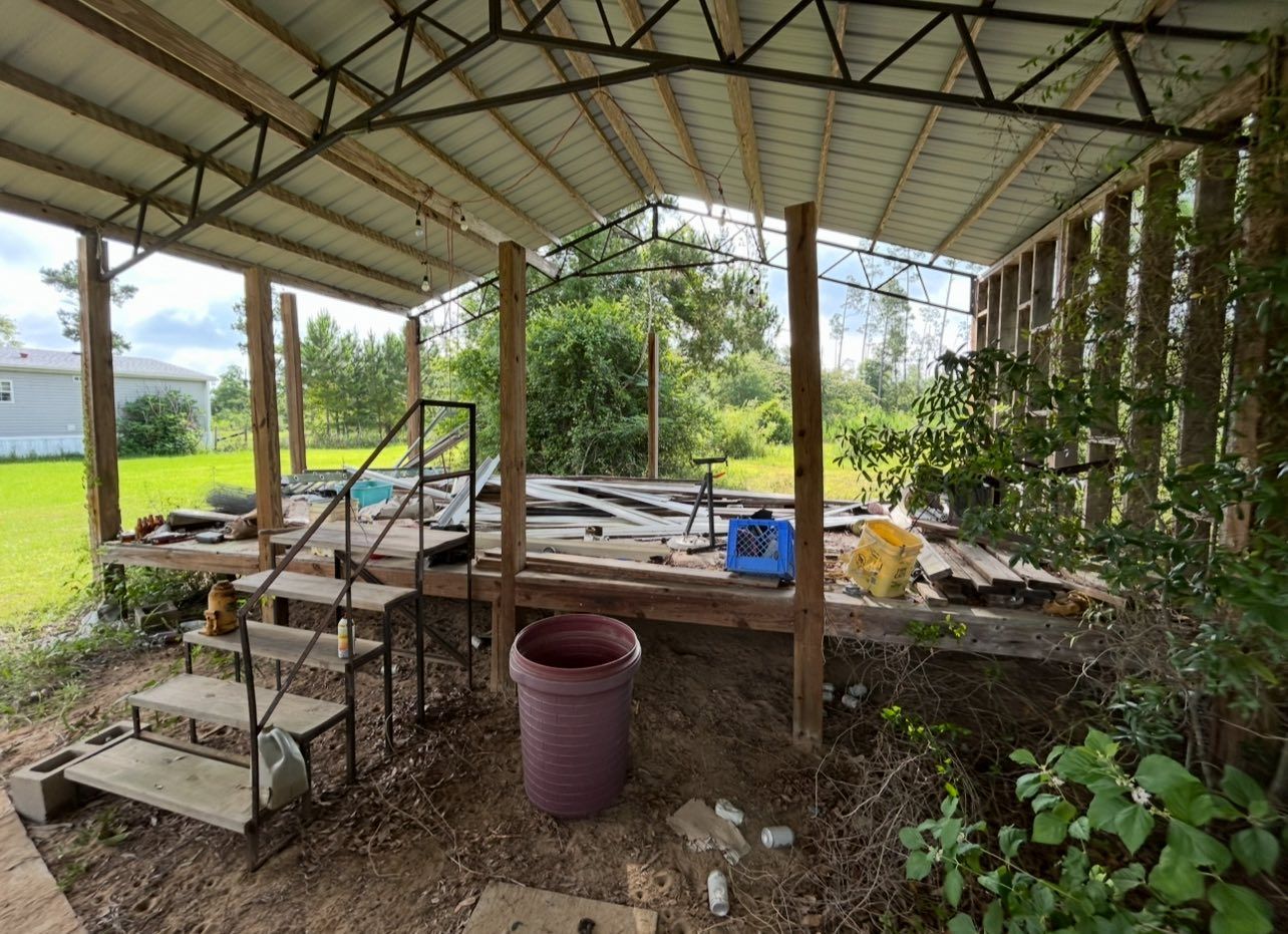Covered wooden platform with steps, metal roof, and surrounding vegetation.