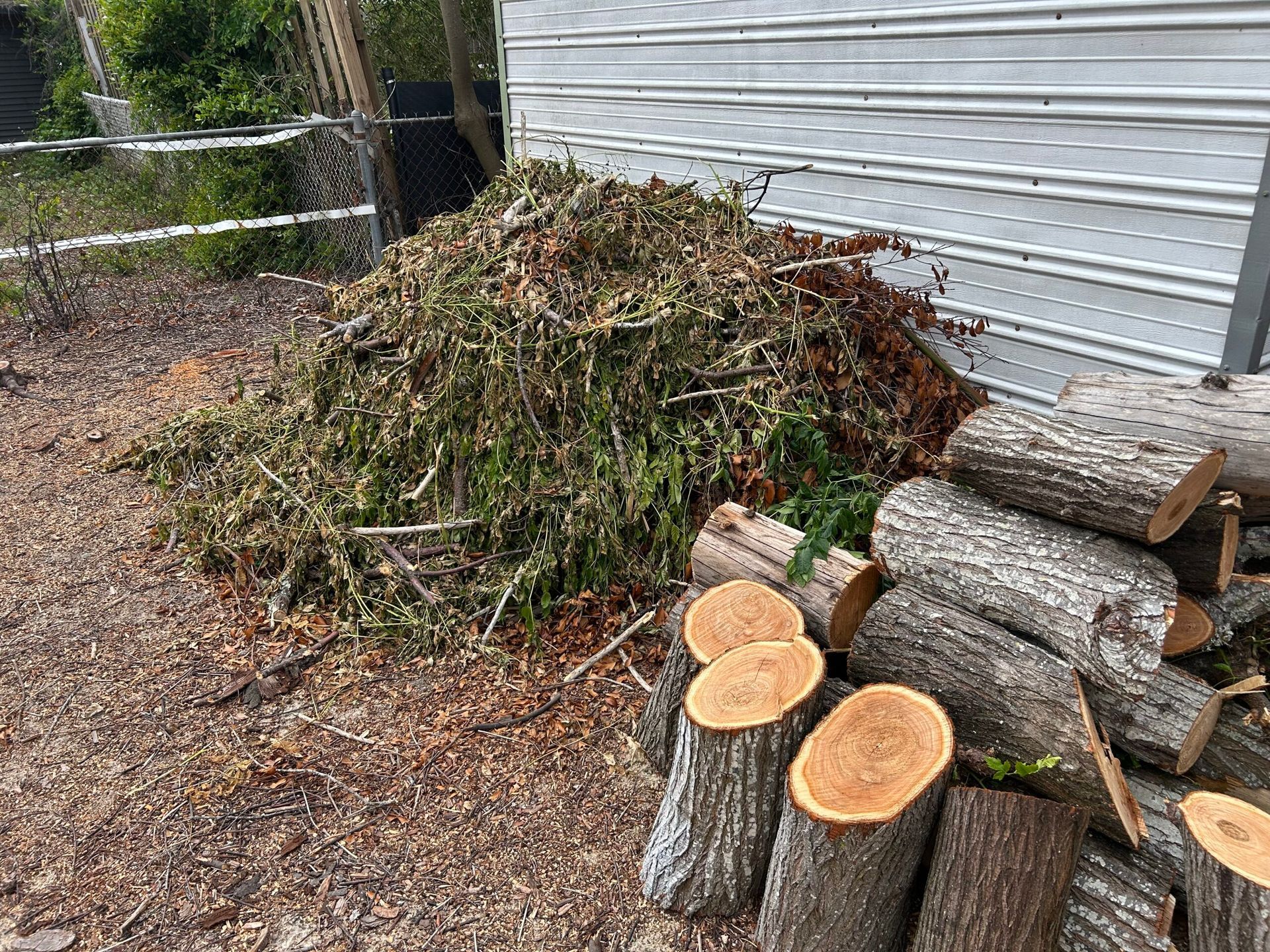 Pile of brush and firewood next to a white sided building.