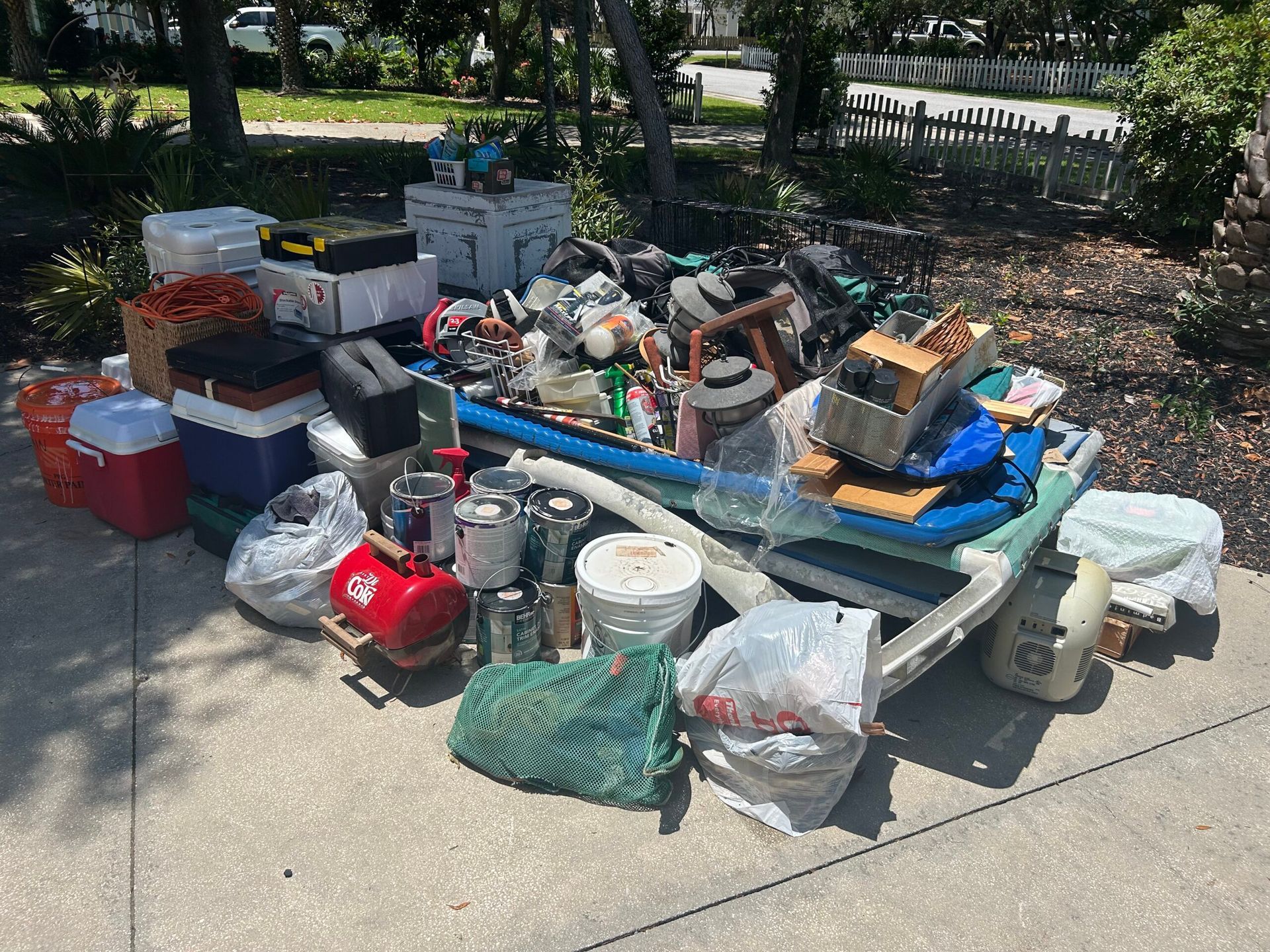 Pile of discarded household items, including appliances, tools, and containers, on a blue sled on a paved surface.