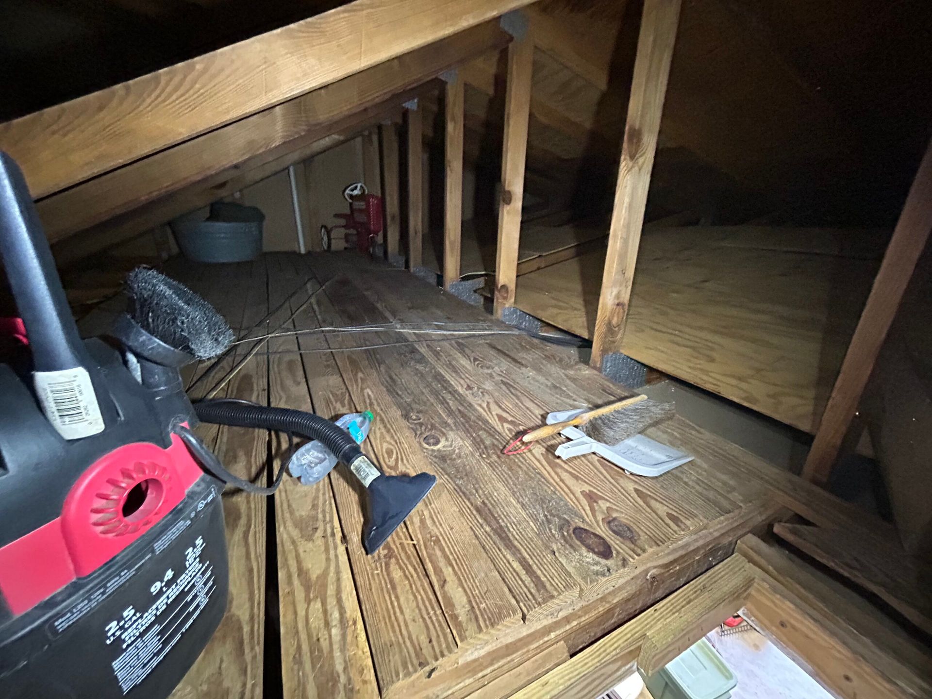 Attic interior with wood flooring, vacuum cleaner, and rafters.