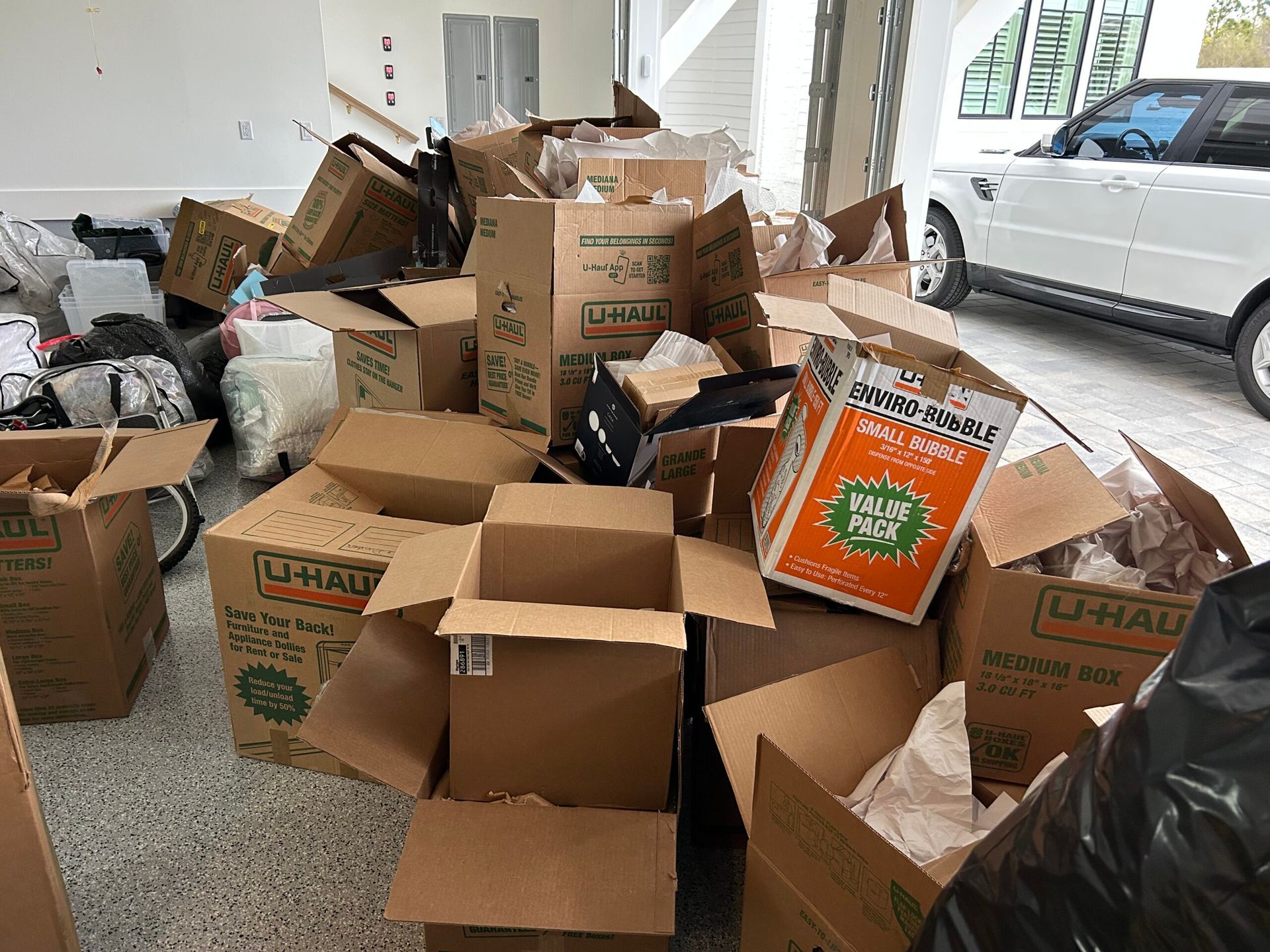Pile of cardboard moving boxes in a garage, next to a white SUV.