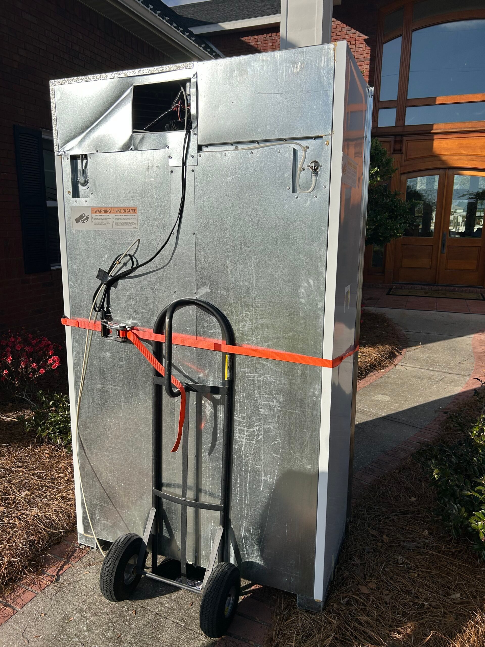 A large metal box secured with orange straps on a hand truck, leaning against a building.