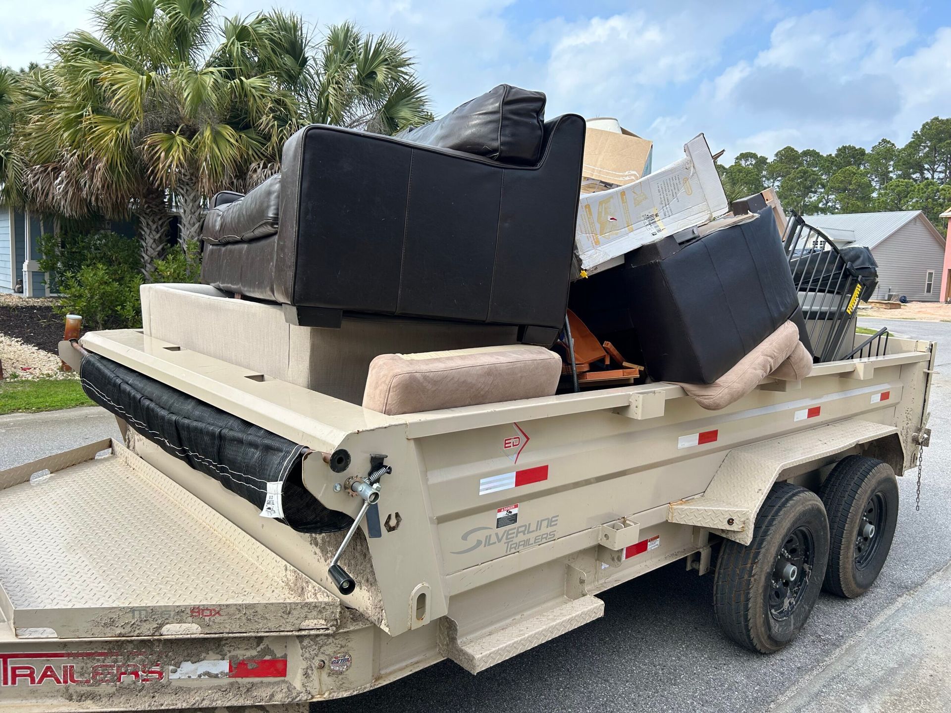 A tan trailer loaded with furniture; a couch, chairs, and other items. The trailer is parked on a road.