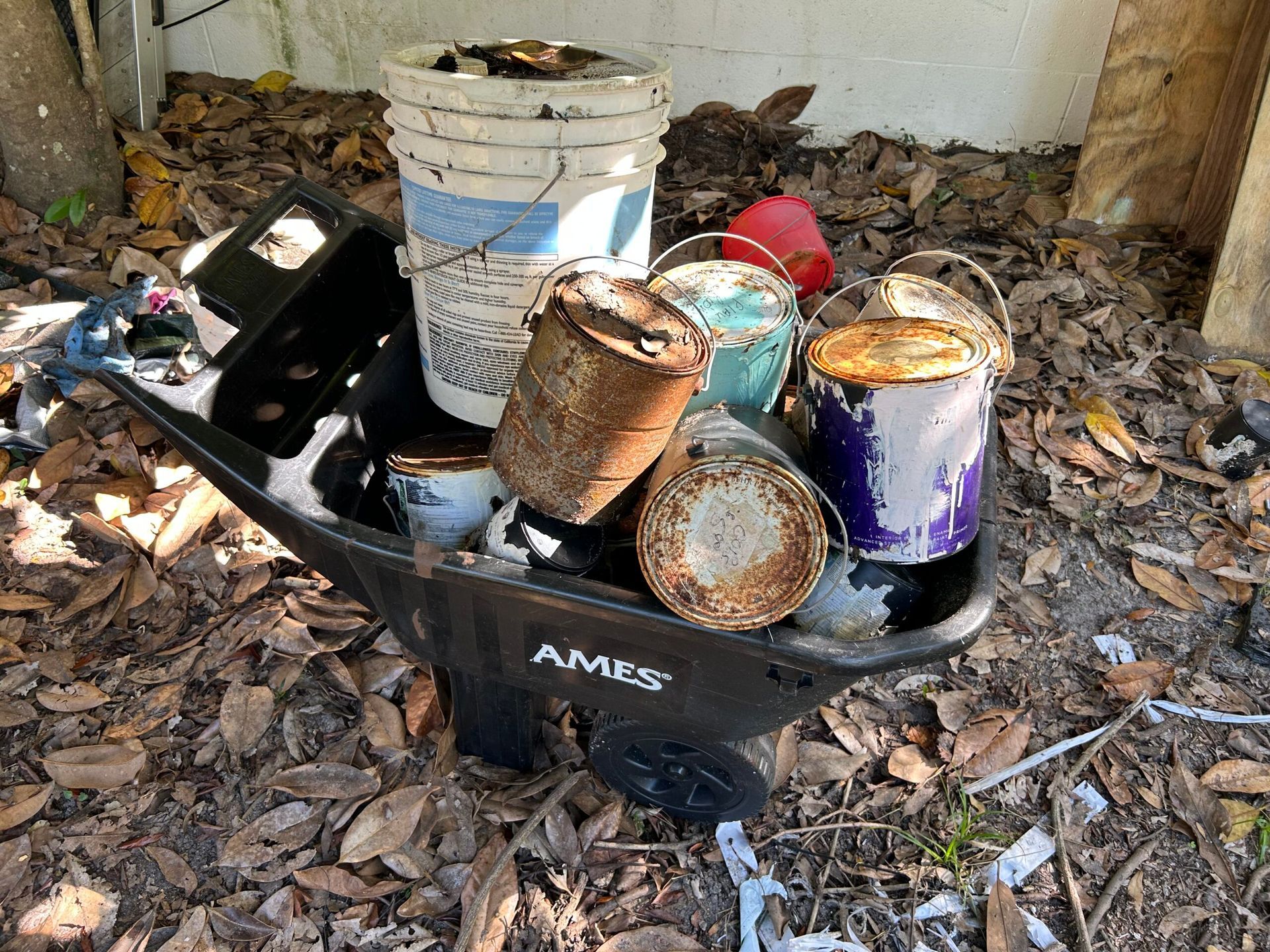 Wheelbarrow filled with paint cans and debris, outdoors in a yard.