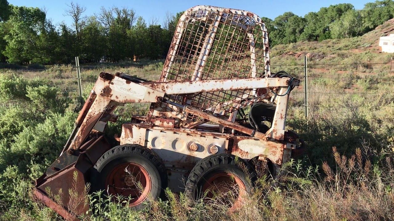 Rusty, abandoned skid steer loader in a grassy field.