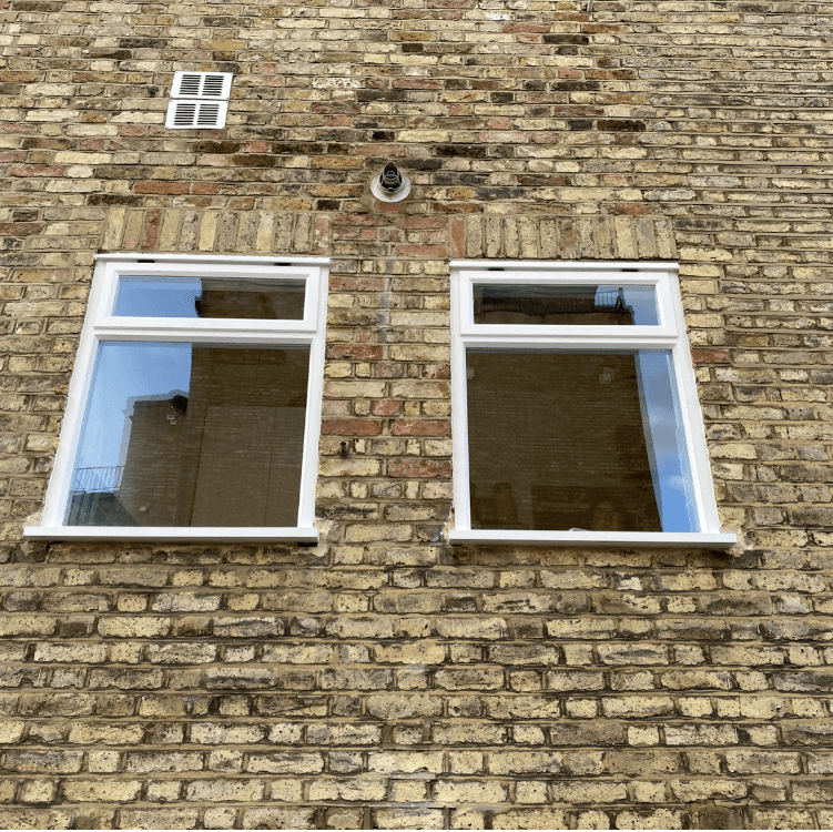 two white sash windows on a brick wall with a reflection