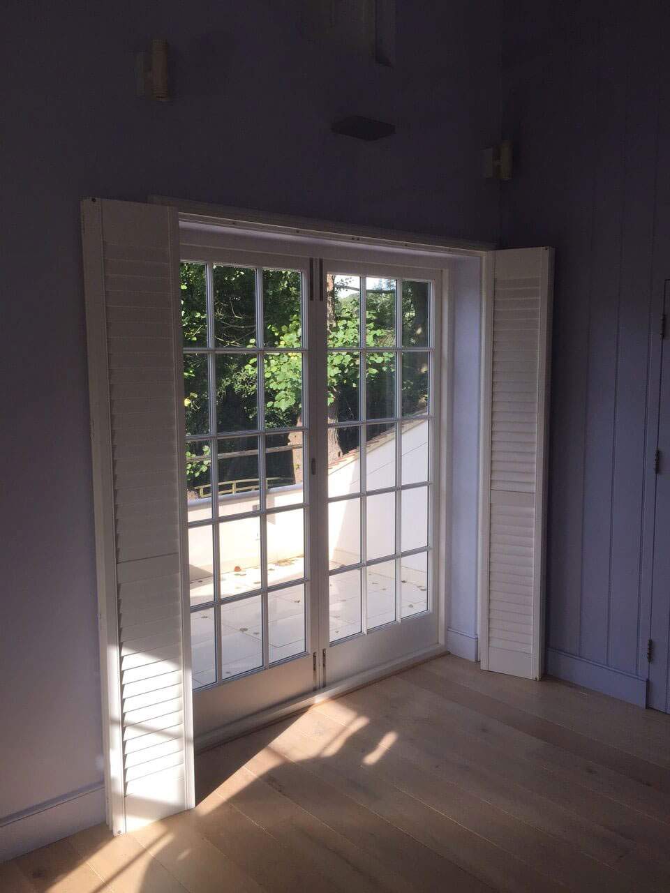 A room with a sliding glass door and white shutters