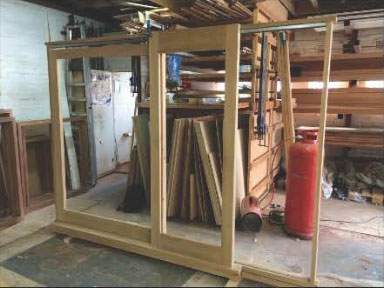 A wooden frame is sitting in a room next to a red gas cylinder.