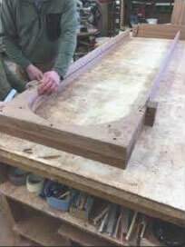 A man is working on a wooden table in a workshop.