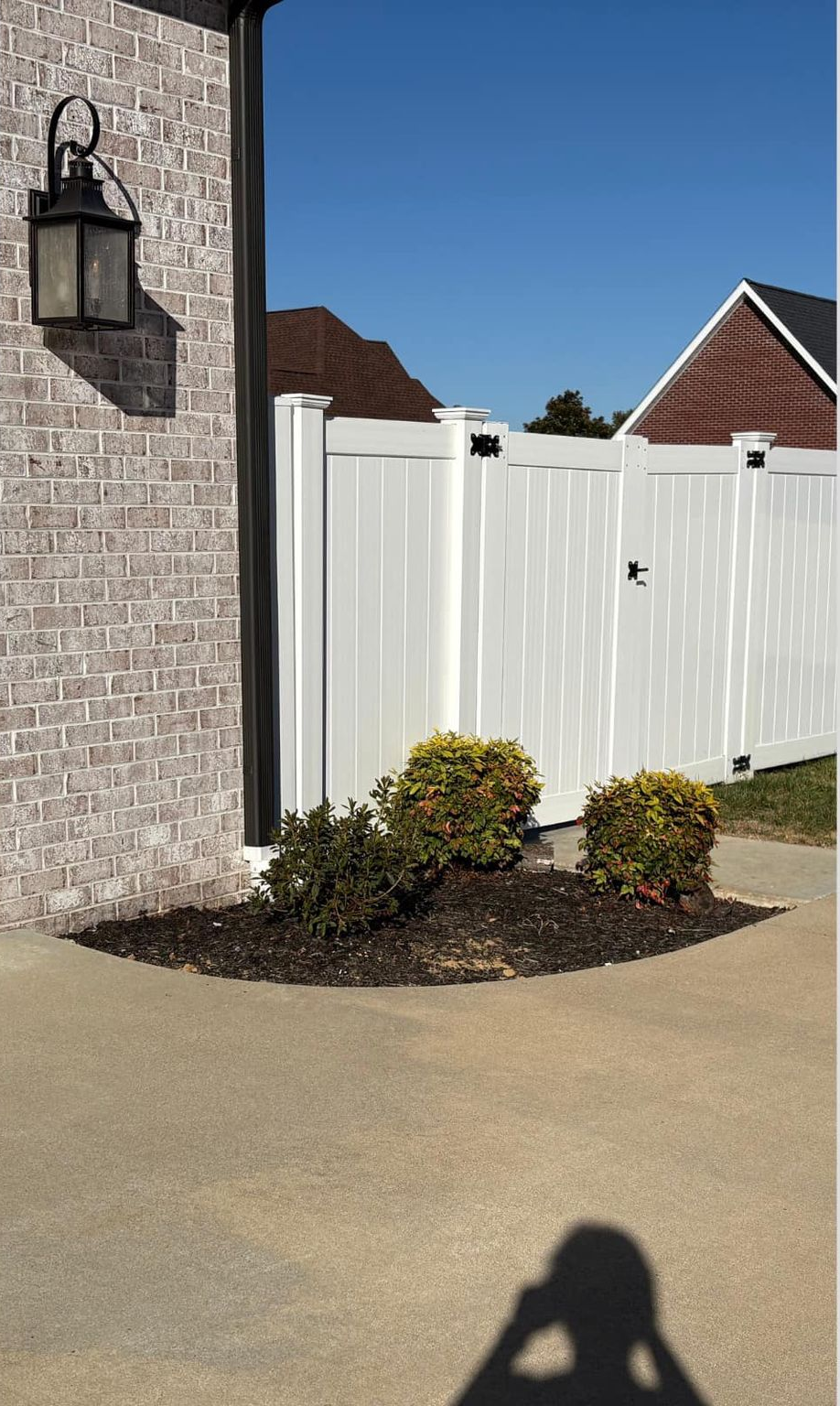 A brick building with a black lantern next to a white fence and a small garden on a sunny day.