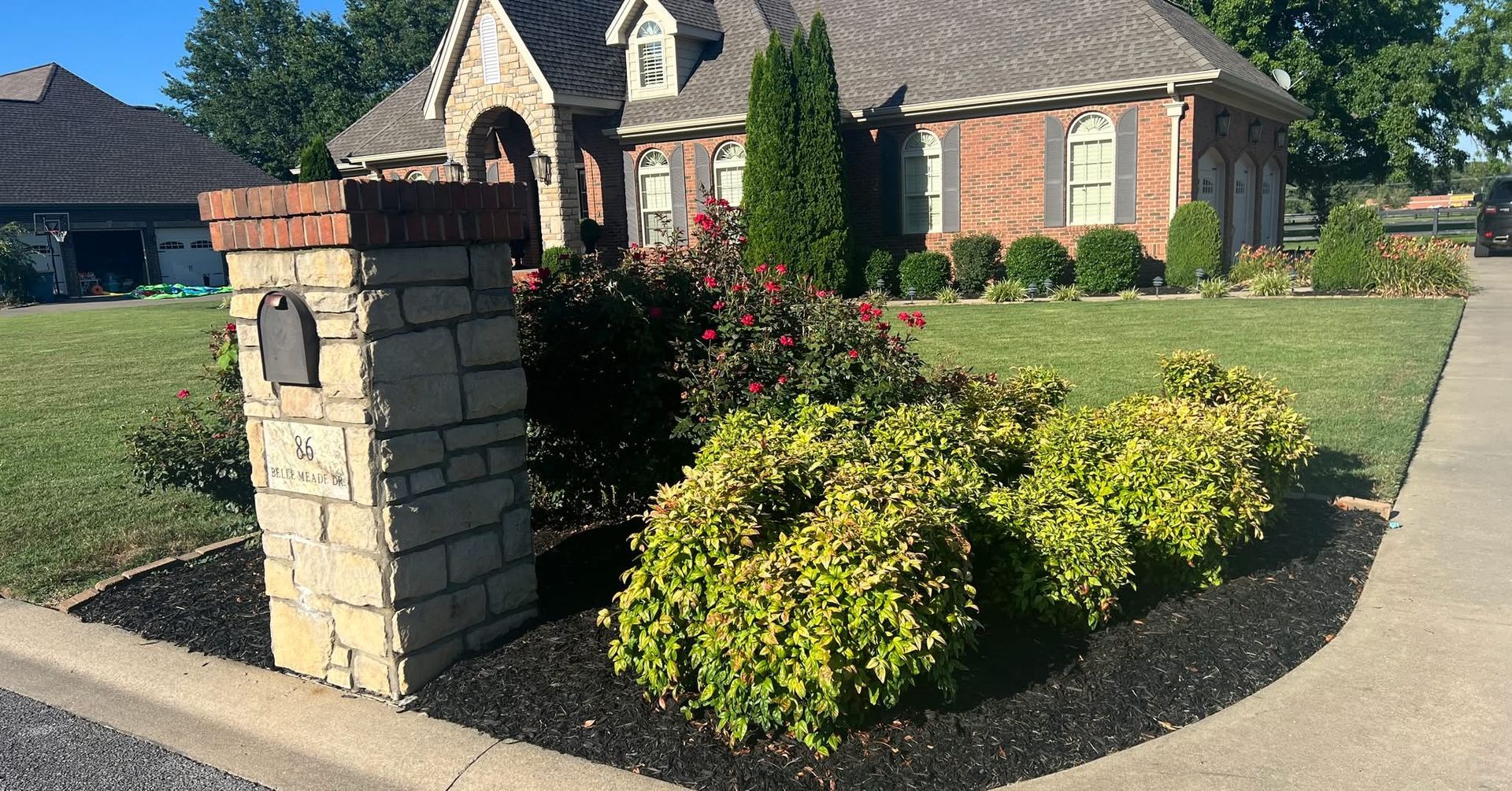 Stone mailbox near a brick house with green lawn and landscaping.