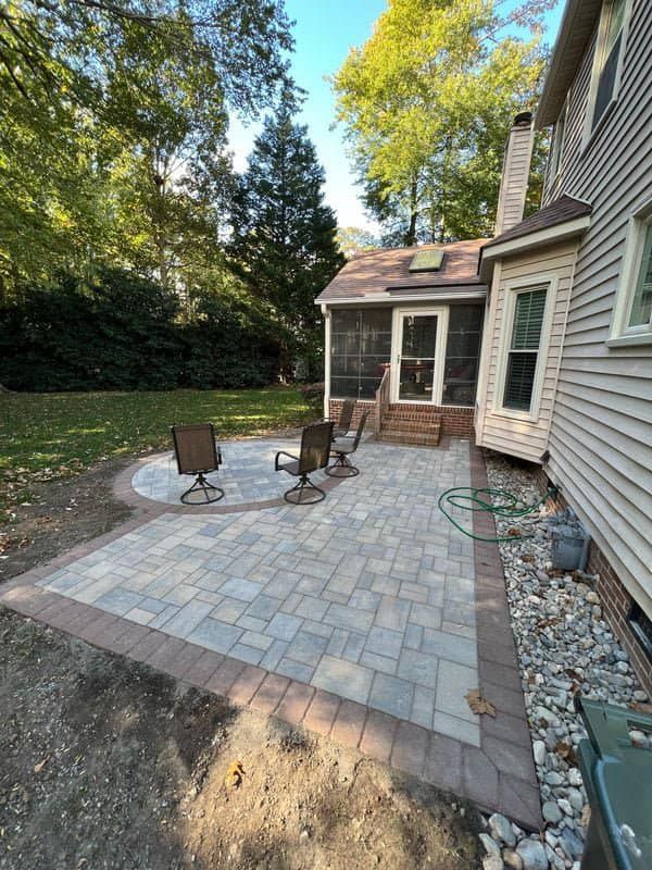 Patio with gray and brown pavers, seating, and a screened porch next to a house.