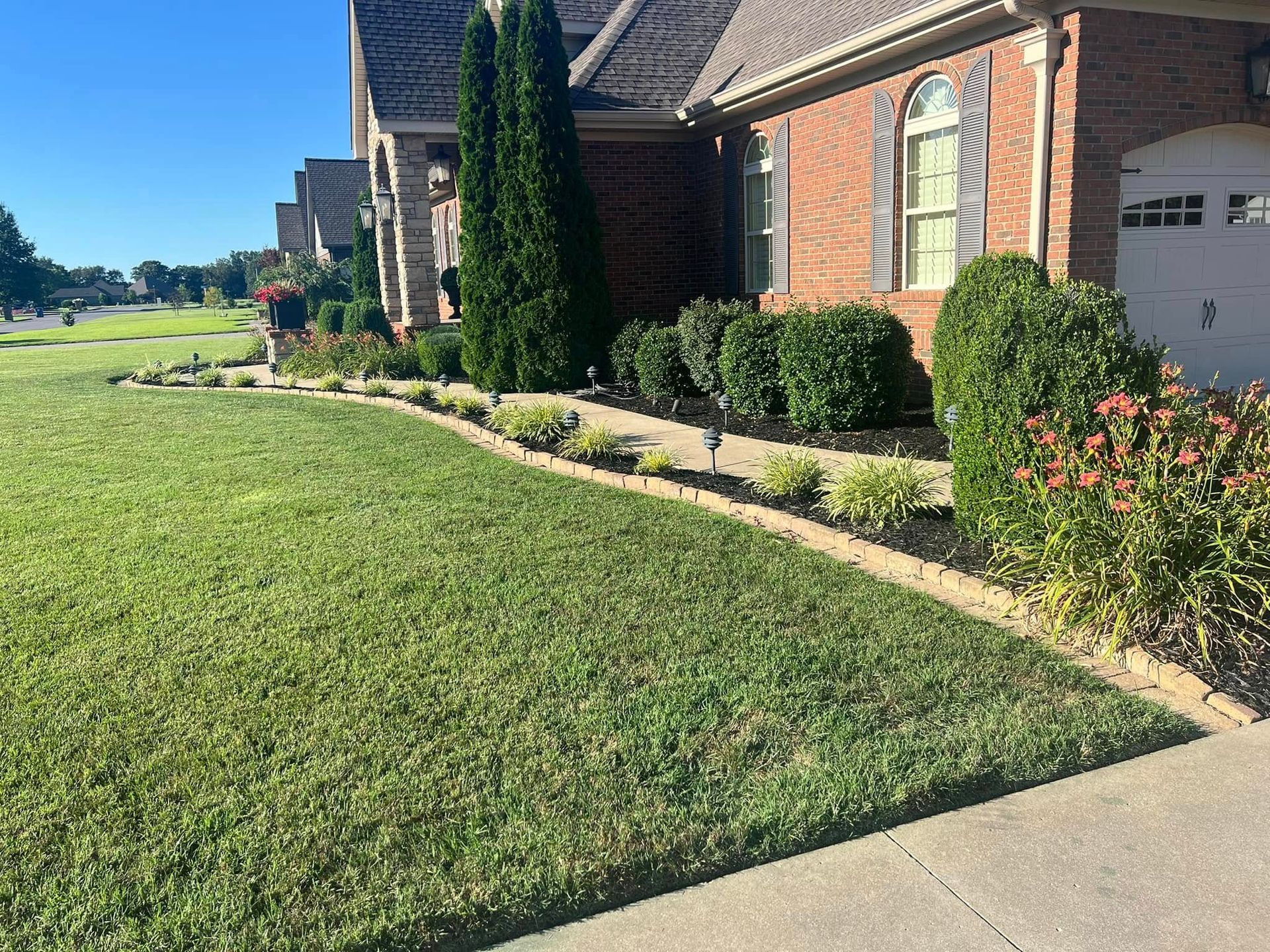 A house with a well-maintained yard and landscaping; green grass, bushes, and brick exterior.