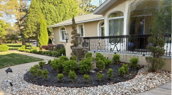 Well-maintained beige house with landscaped front yard, circular garden bed, fountain, and decorative rock border.
