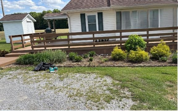 A house with a wooden ramp and flowerbeds in front. Gravel driveway and green lawn.