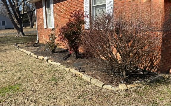 Red brick house with a brown shrub border, and dry grass.