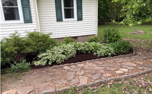 Stone path leading to house with landscaped garden beds of green and white foliage.