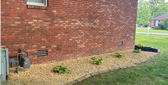 Red brick house exterior with a gravel bed border, small plants, and green grass.