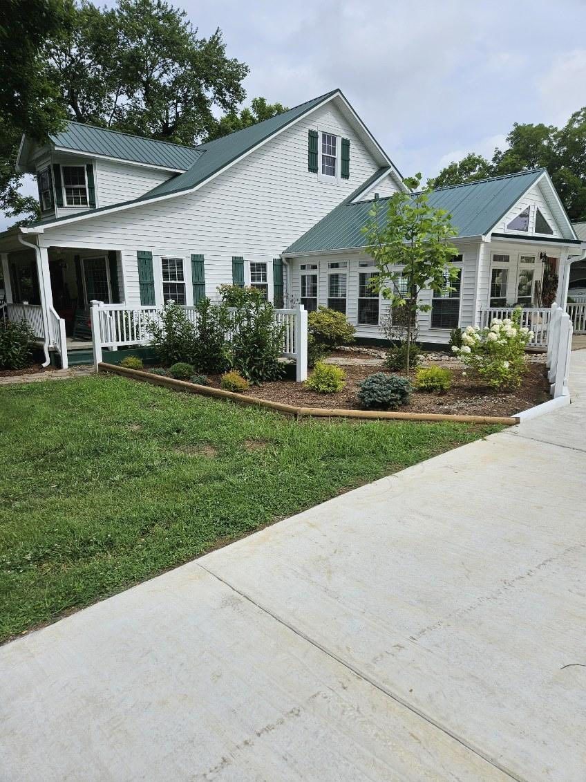 White house with green shutters, roof, and landscaping. Concrete walkway in front.