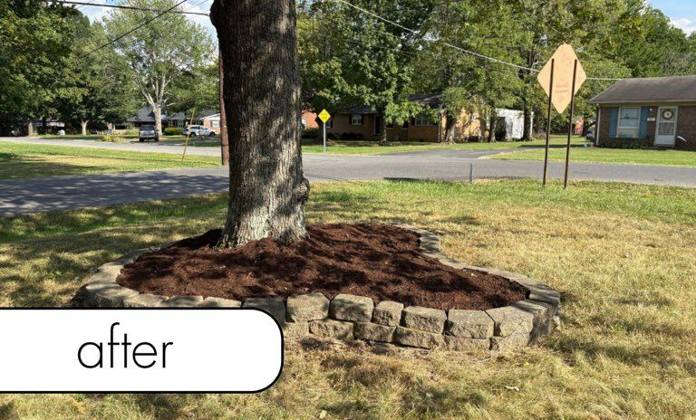 White fence with dark mulch bed, small bushes, brick wall, and blue sky.