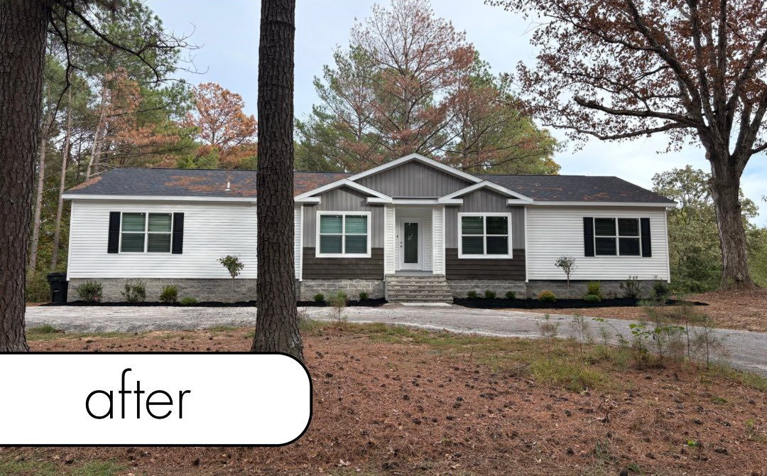 White fence with dark mulch bed, small bushes, brick wall, and blue sky.