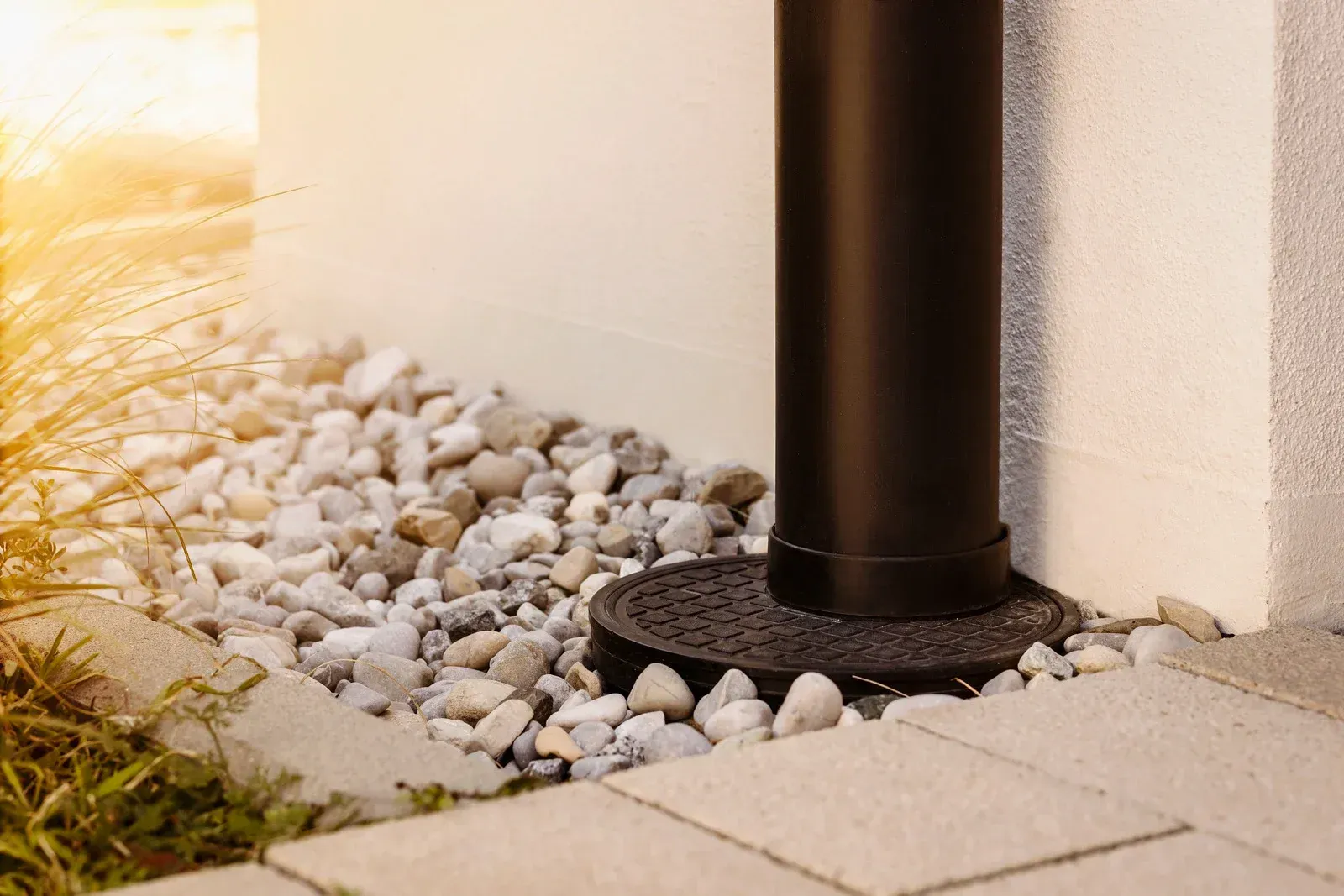 Black pole base set on dark stone circle, surrounded by pebbles next to a white wall and stone pavers.