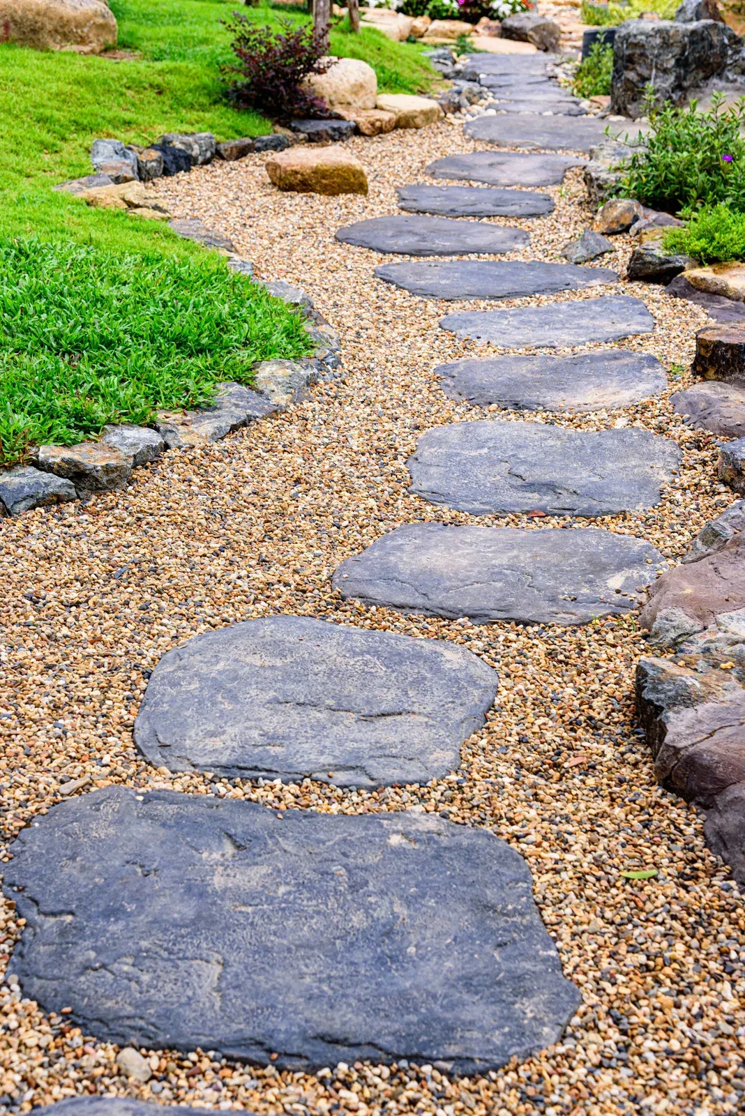 Stone path through a garden with gravel and greenery.