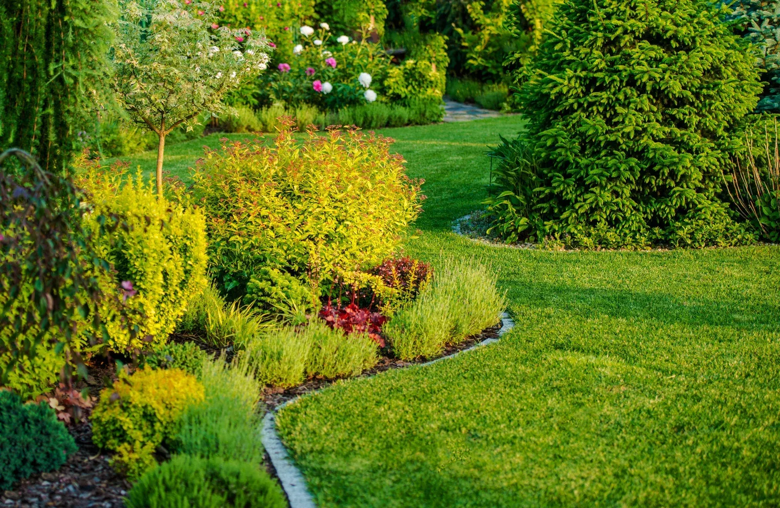 Lush green garden with manicured lawn, various shrubs, and colorful plants.