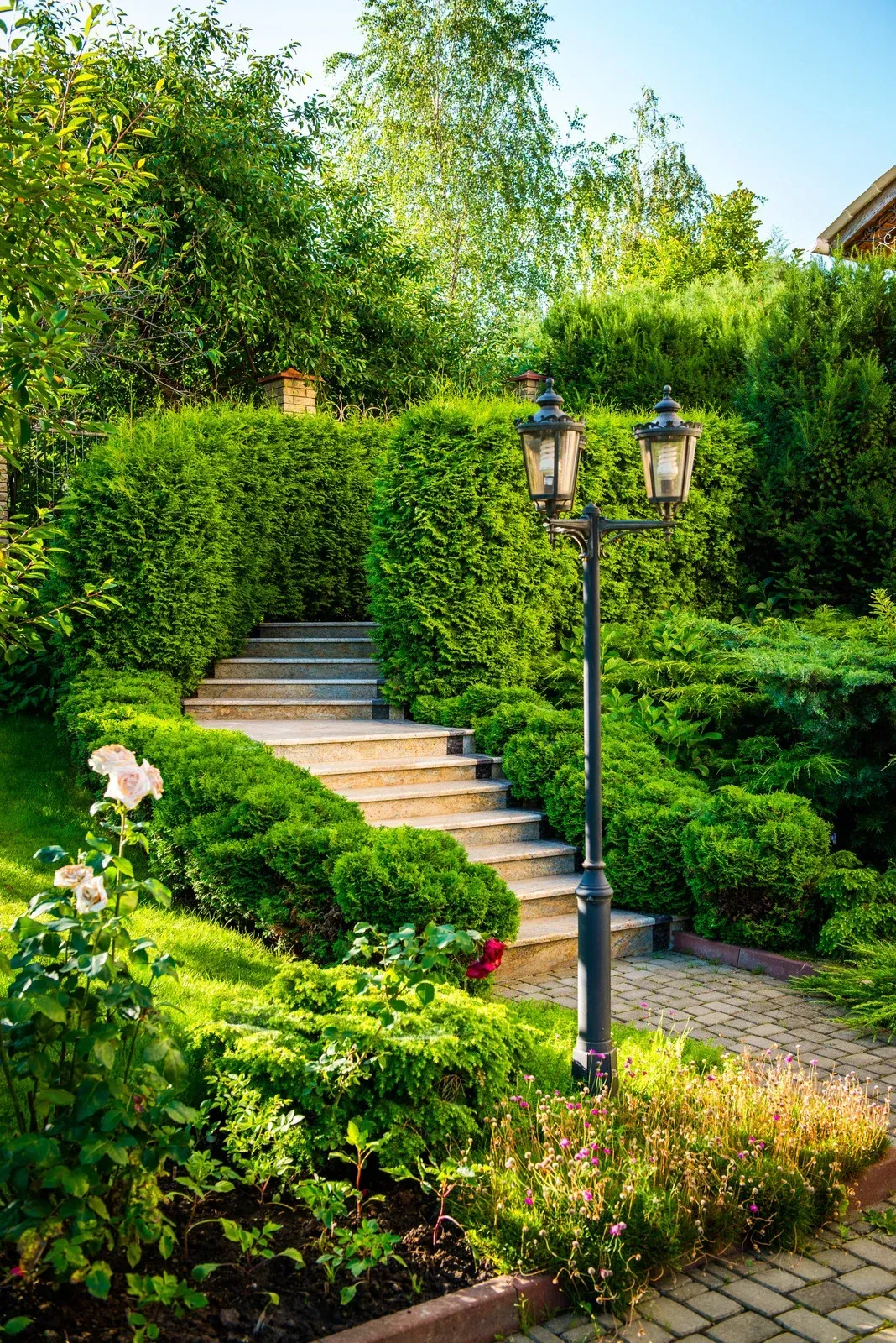 Stone steps ascend through a manicured garden with lush greenery and a vintage lamppost.