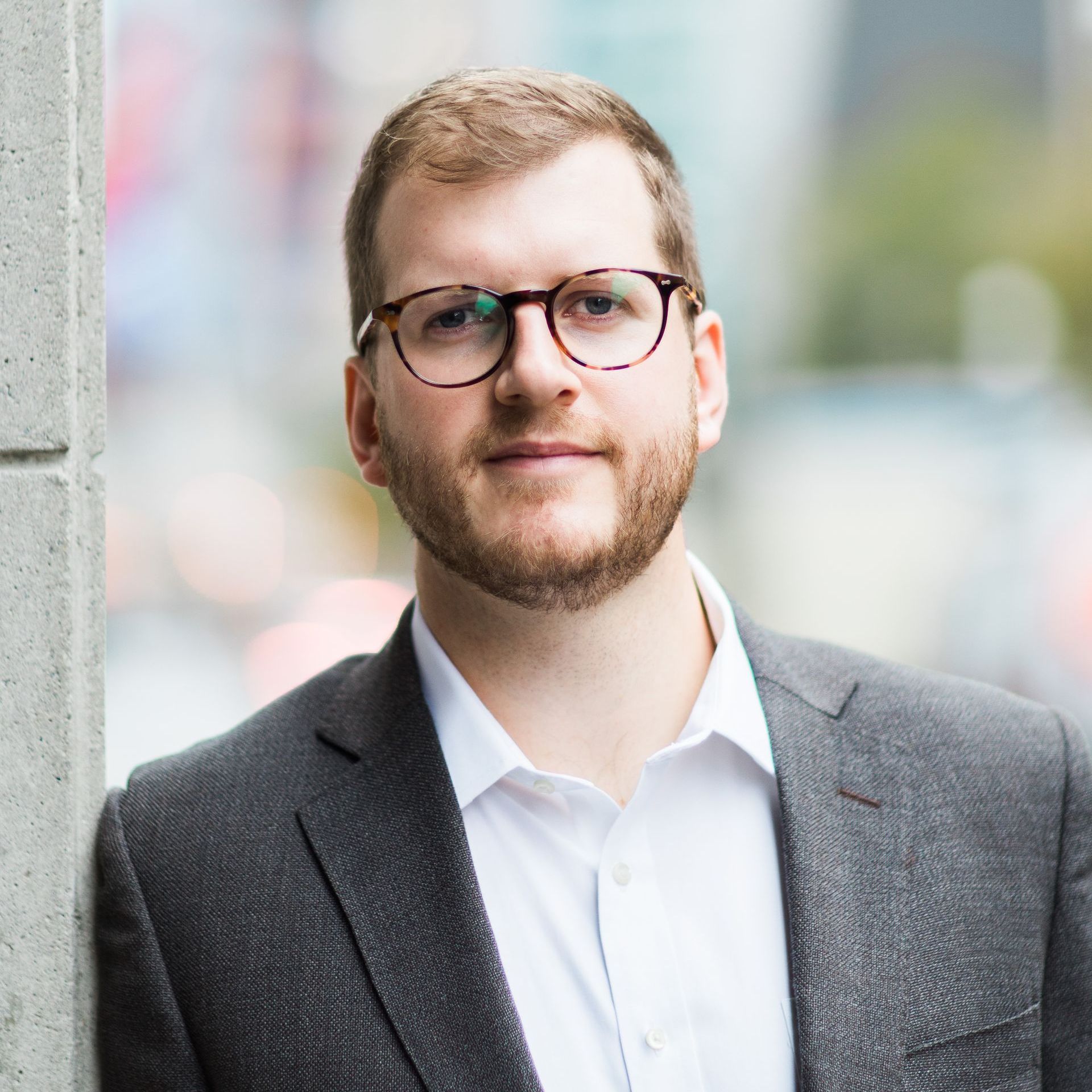 A man in a suit and glasses is standing on a city street.